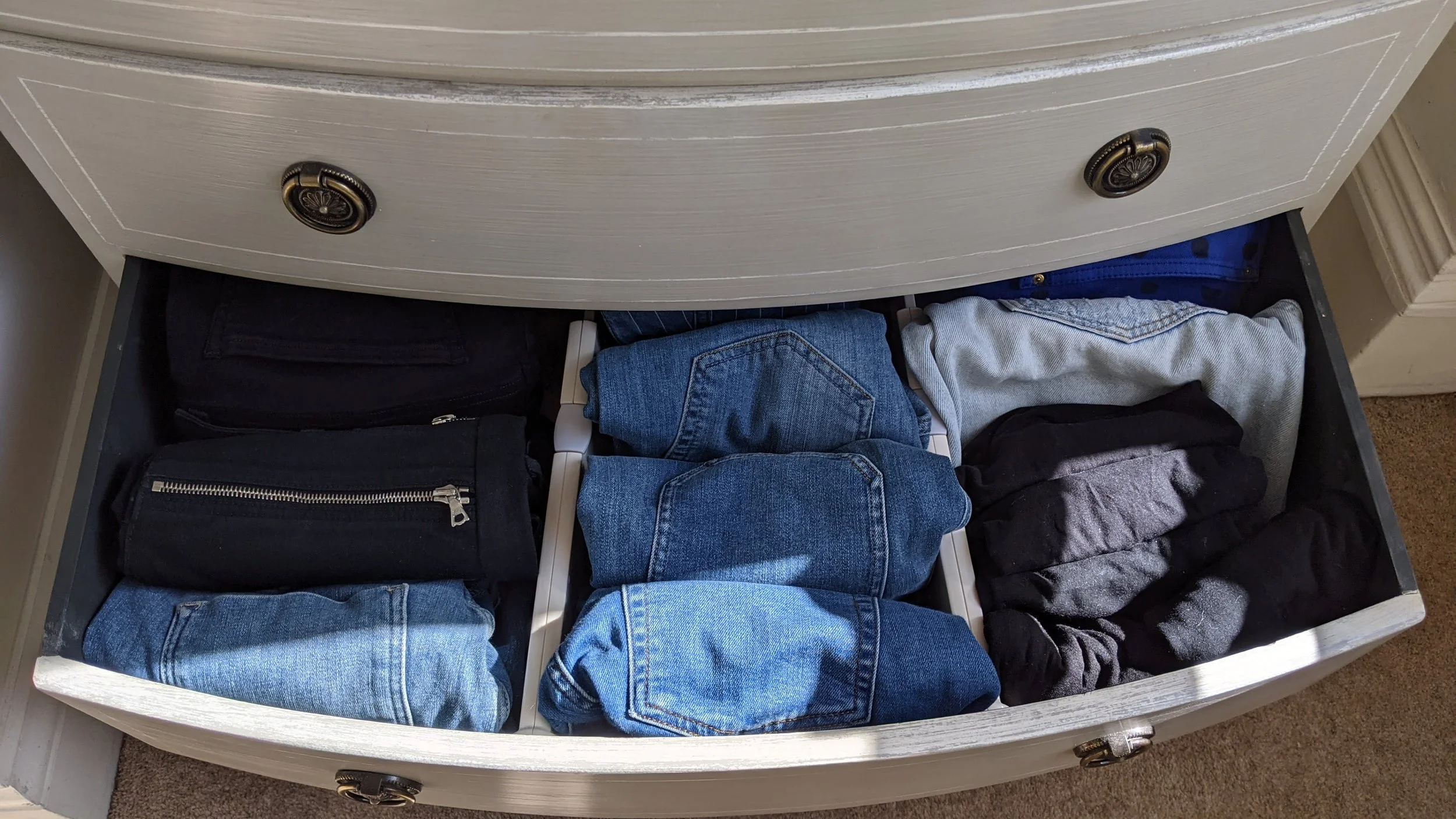 Open drawer containing folded pants and jeans, with some in black, blue, gray, and black with gray.