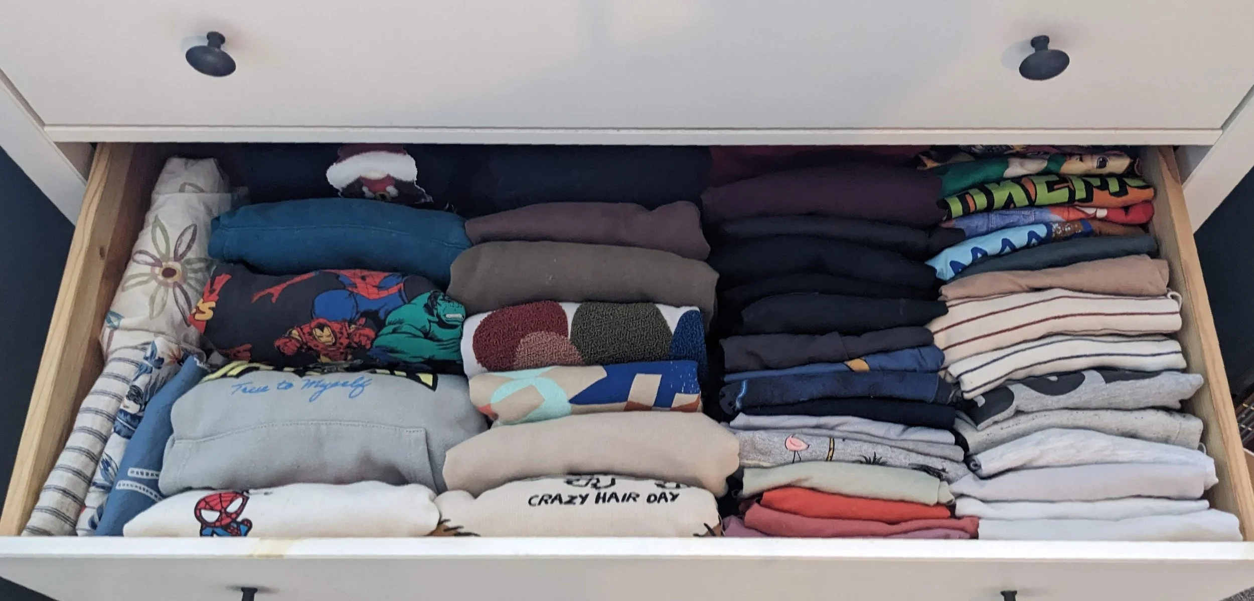 Open drawer filled with neatly folded t-shirts and clothes of various colors and patterns.