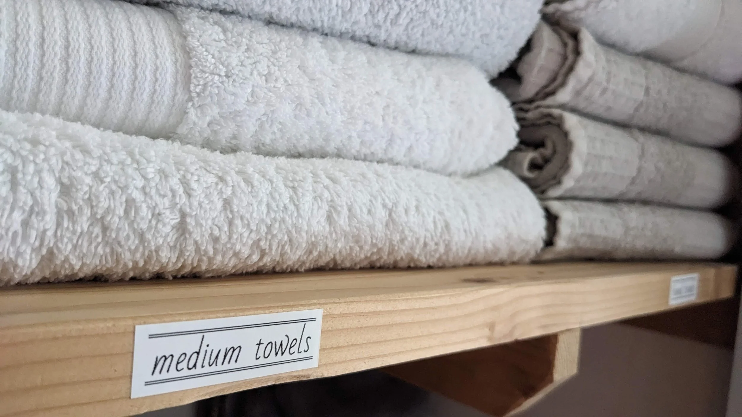 A shelf with neatly folded medium-sized towels, mostly white, with a label that reads 'medium towels' in black text.