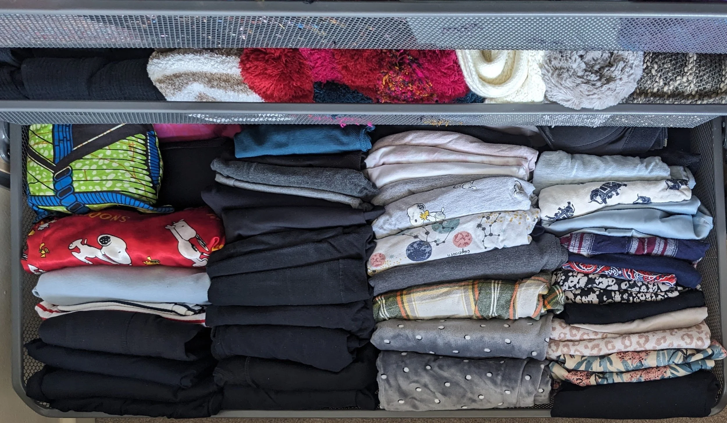 Clothes organized in a metal drawer, including folded shirts, pajamas, and various textile items.