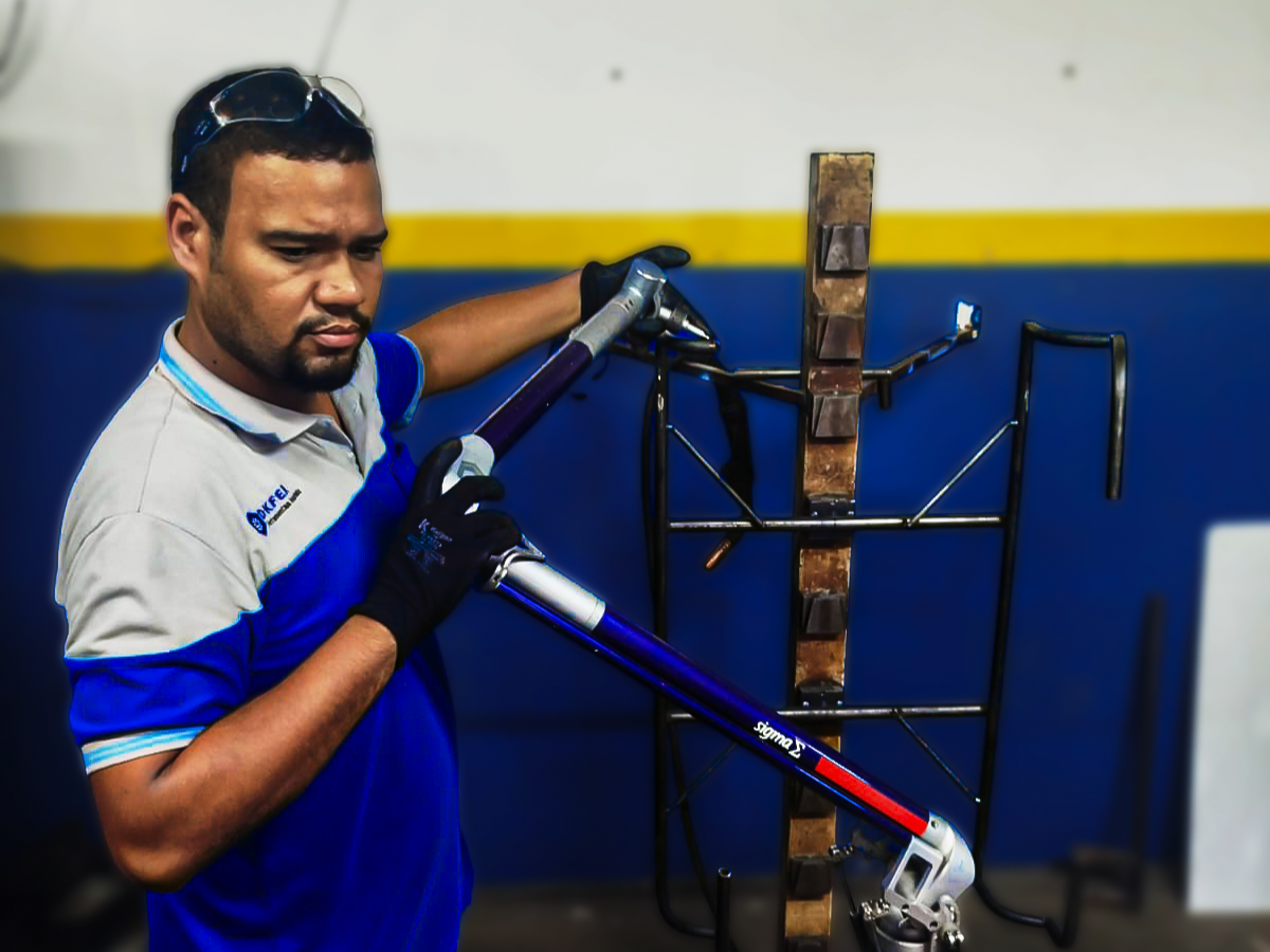 Homem usando uma robot de solda com uma arma de solda em uma oficina, vestindo luvas pretas e uma camisa de trabalho