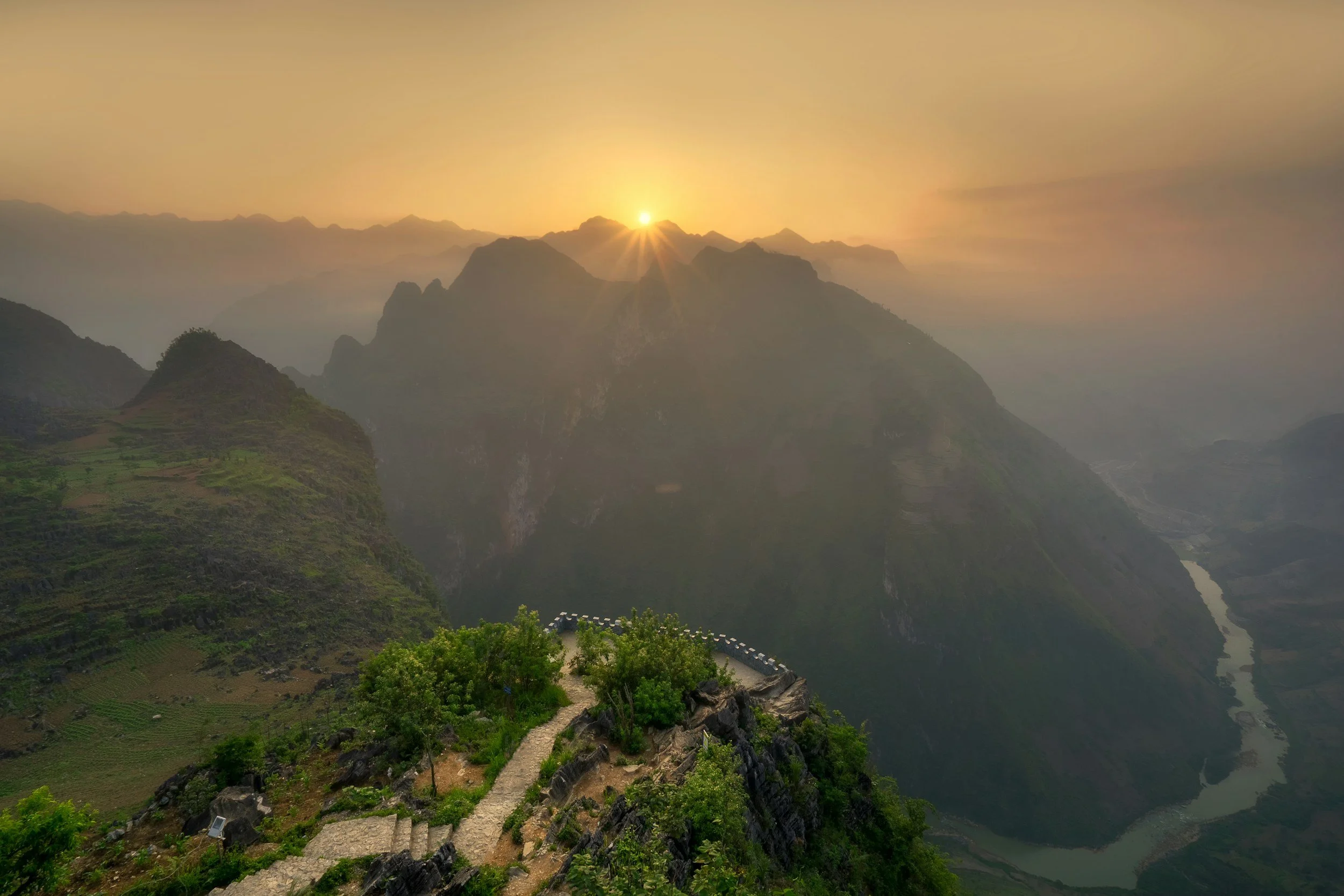 Sunrise on the Inca Trail overlooking Andean mountains with a pathway and greenery in the foreground.