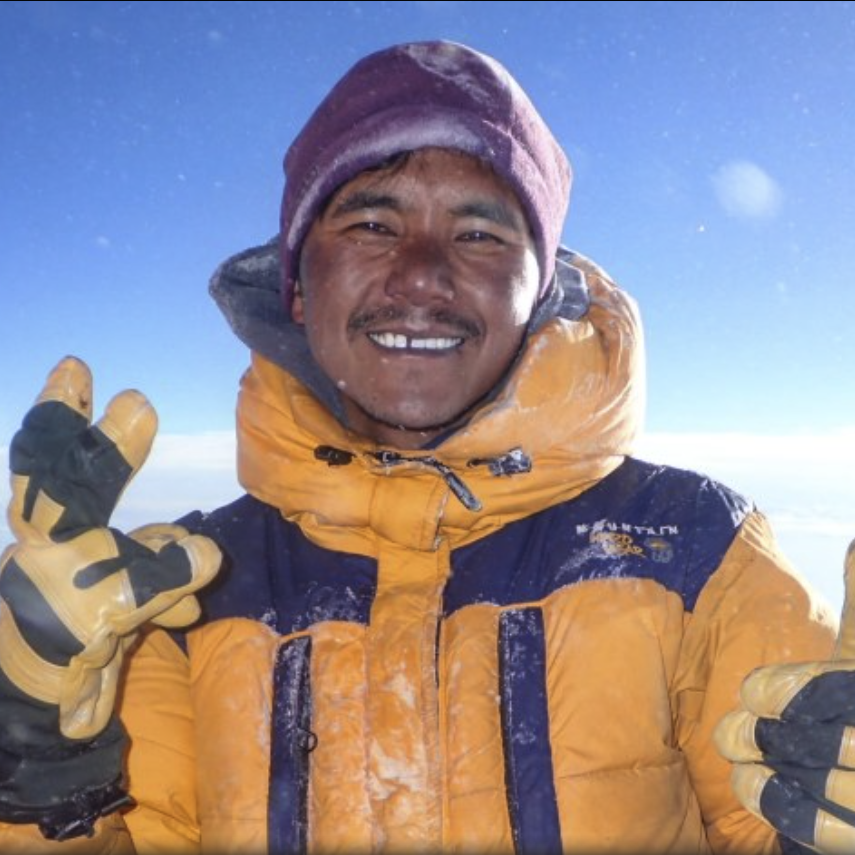 Rugged Luxury guide, Pega Sherpa, stands smiling in his summit suit on Everest. 