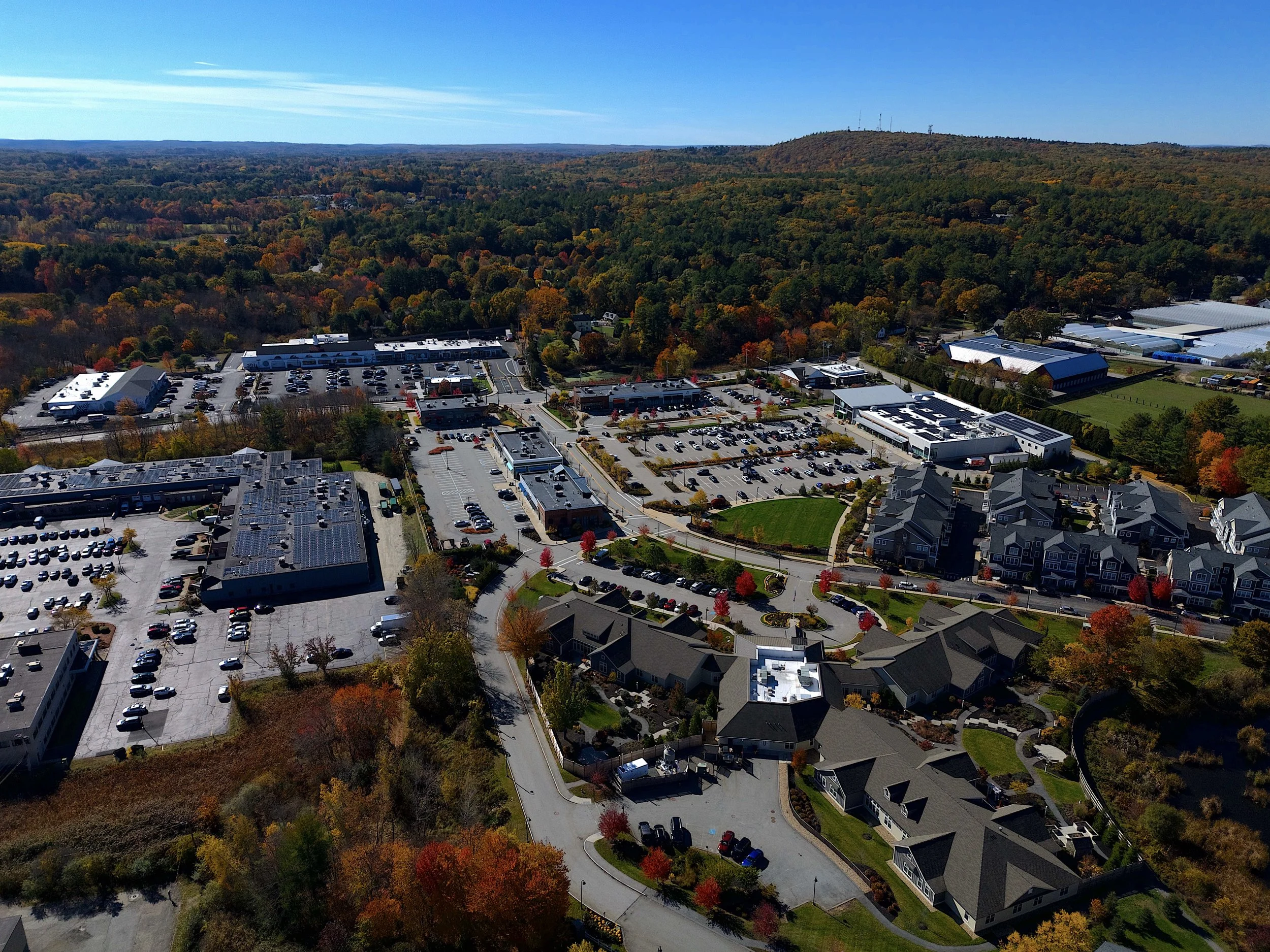 Real estate, marketing aerial, drone photography of an assisted living facility in Sudbury, Massachusetts with blue skies, mountains, foliage, Boston in a commercial and residential neighborhood.