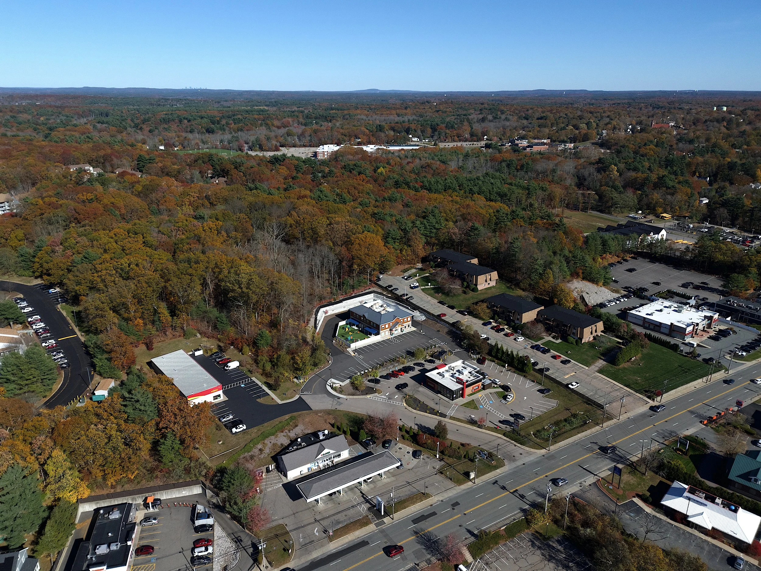 Marketing aerial, drone photo in the town of Franklin, Massachusetts of a day care center with blue skies, foliage and highways with commercial property surrounding the day care center.
