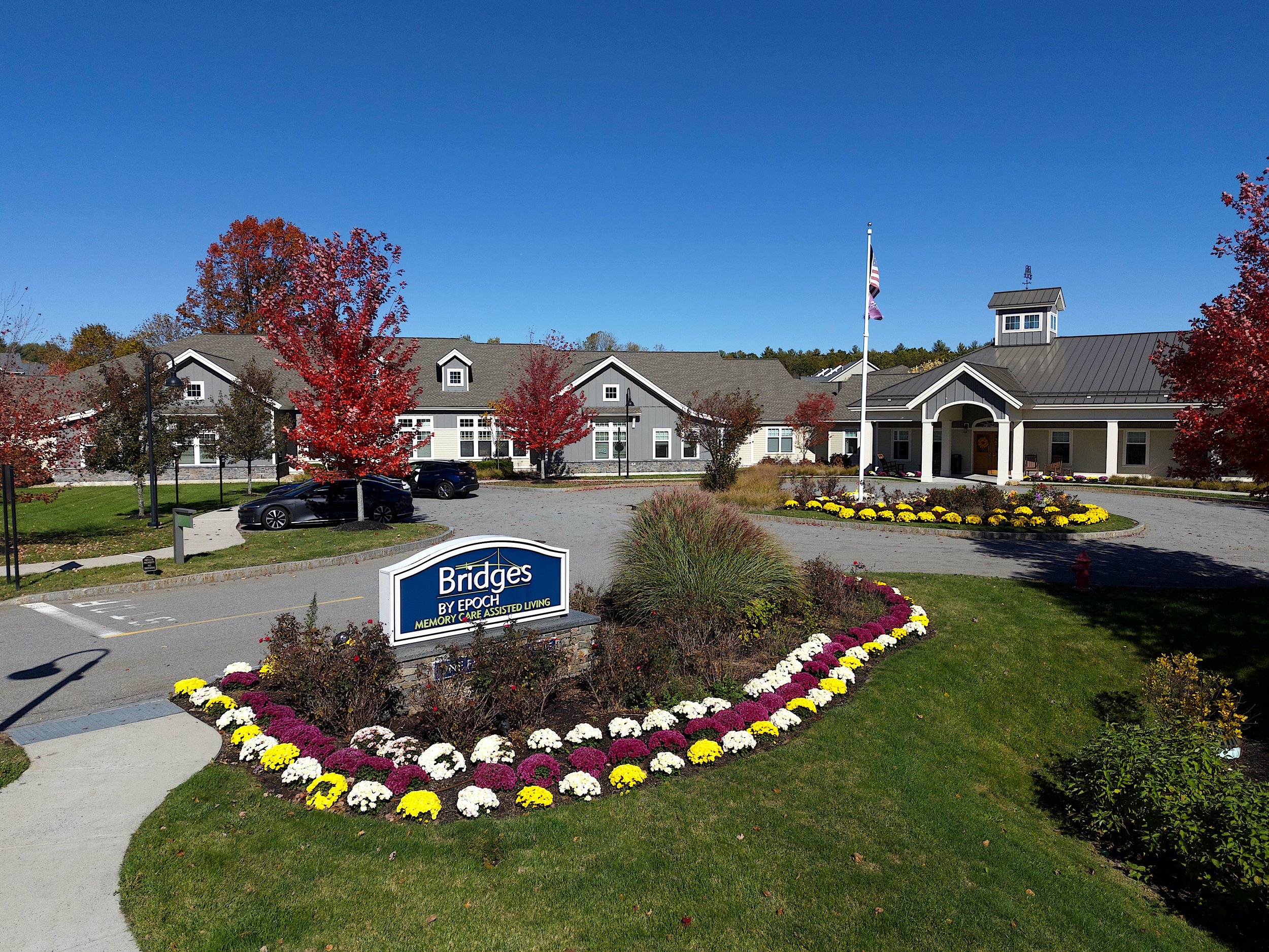 Real estate, marketing aerial, drone photography of an assisted living facility in Sudbury, Massachusetts with blue skies, mountains, foliage, Boston in a commercial and residential neighborhood.