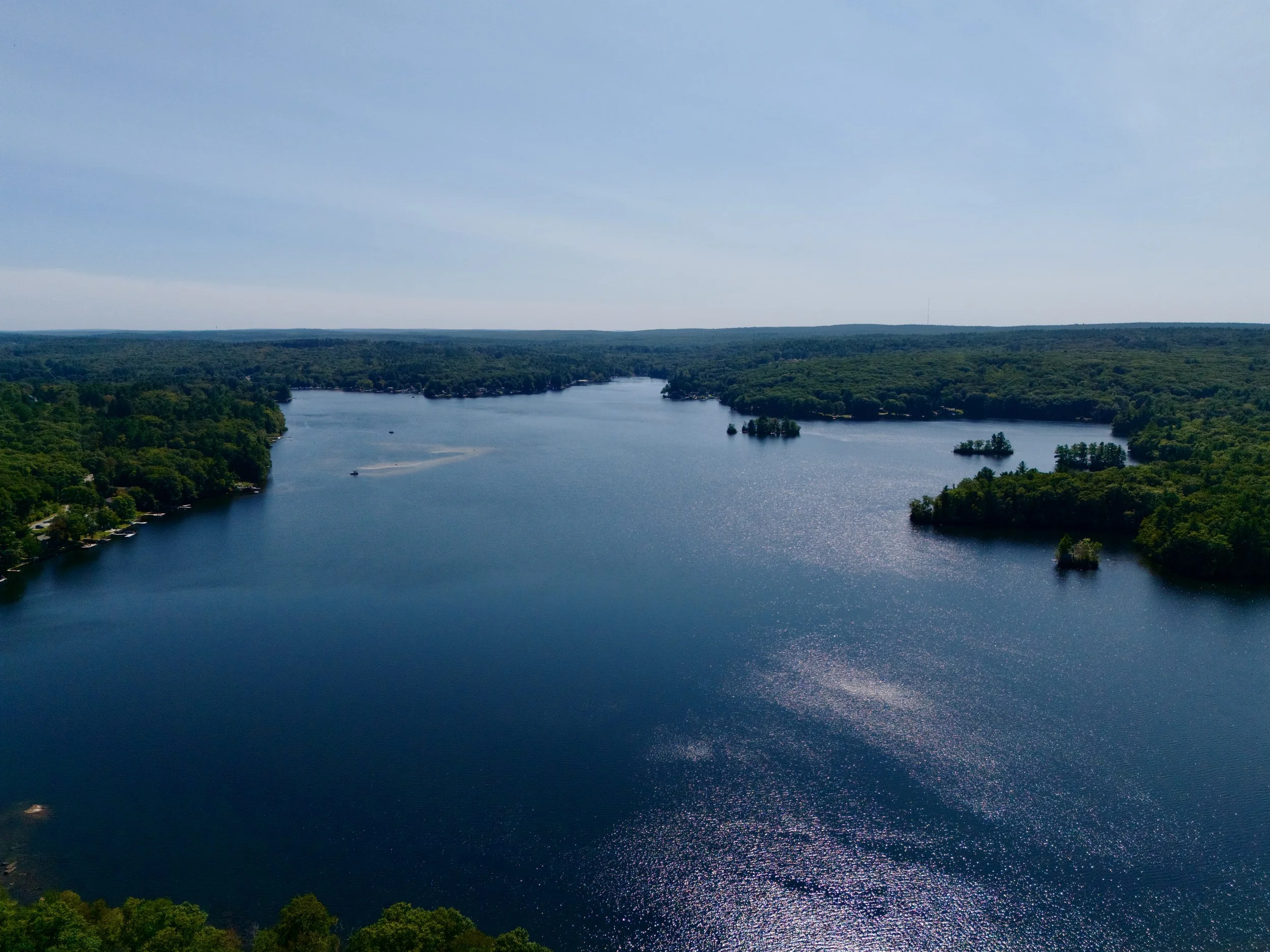 Altitude Drone Dynamics. Horizon view of a large lake in Central Massachusetts surrounded by dense green forests under a clear blue sky. Great boating day.