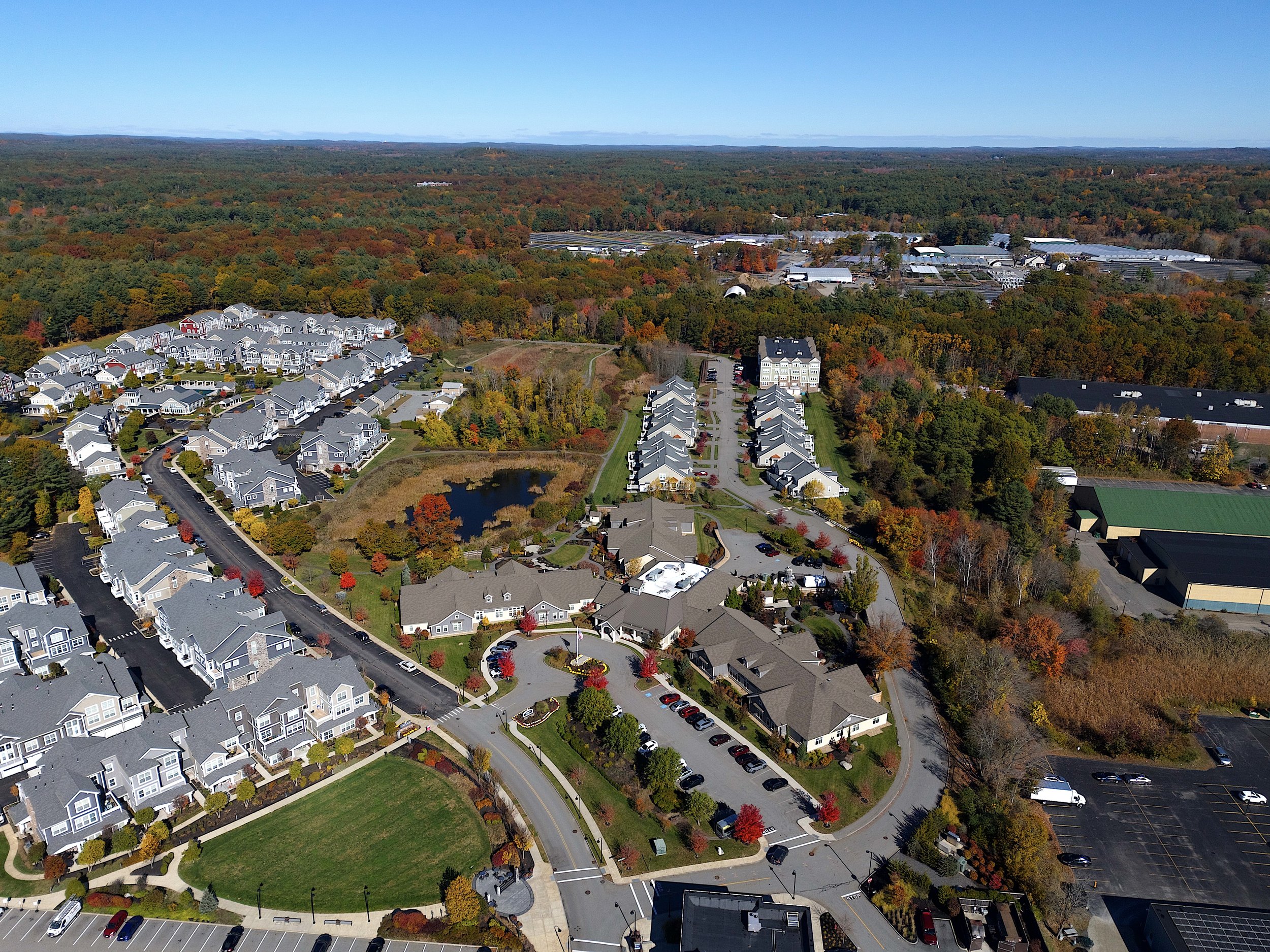 Real estate, marketing aerial, drone photography of an assisted living facility in Sudbury, Massachusetts with blue skies, mountains, foliage, Boston in a commercial and residential neighborhood.