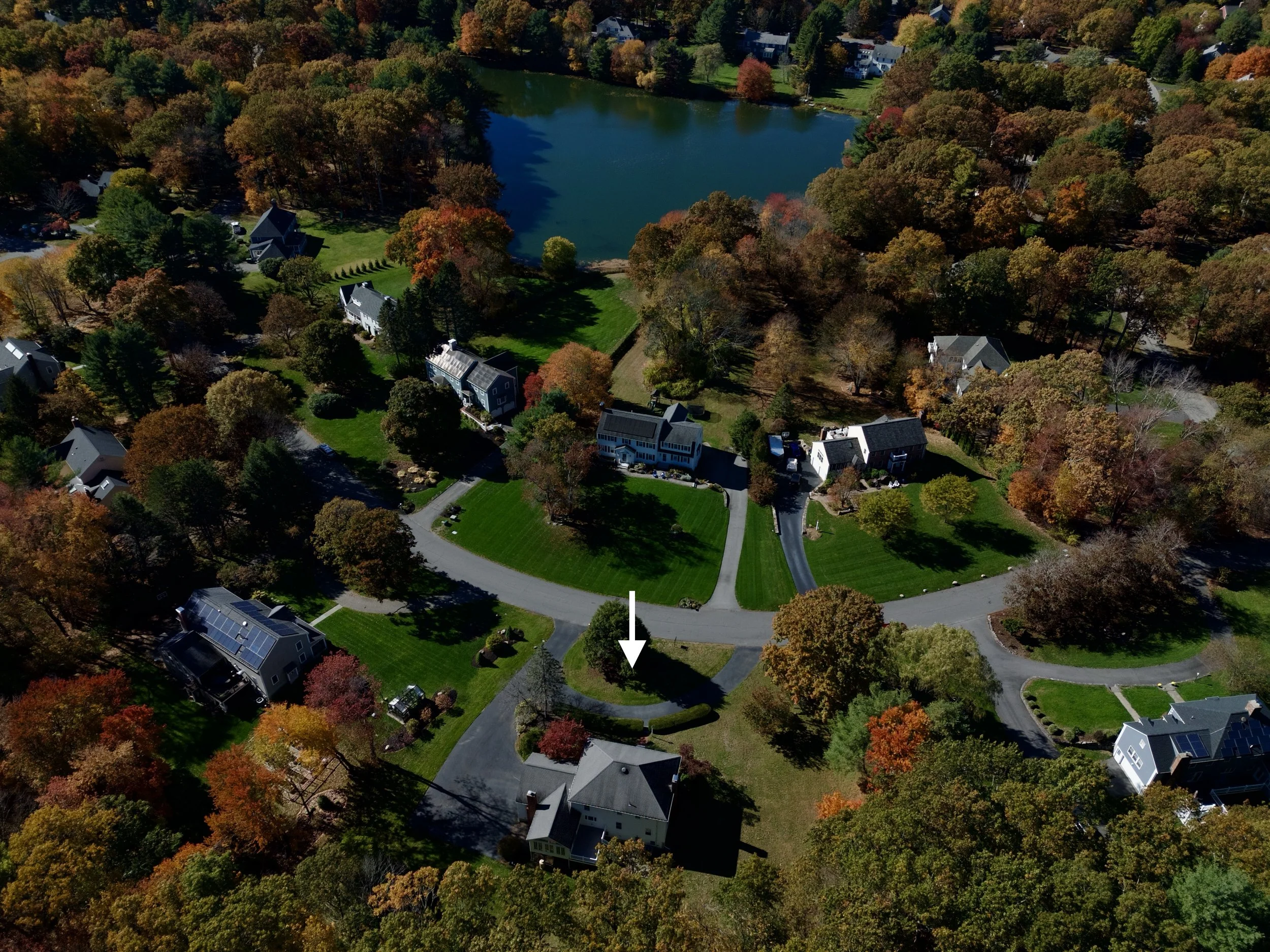 Real estate aerial, drone photography of a house in Sudbury, Massachusetts in a residential neighborhood with blue skies, a lake and foliage near Boston.