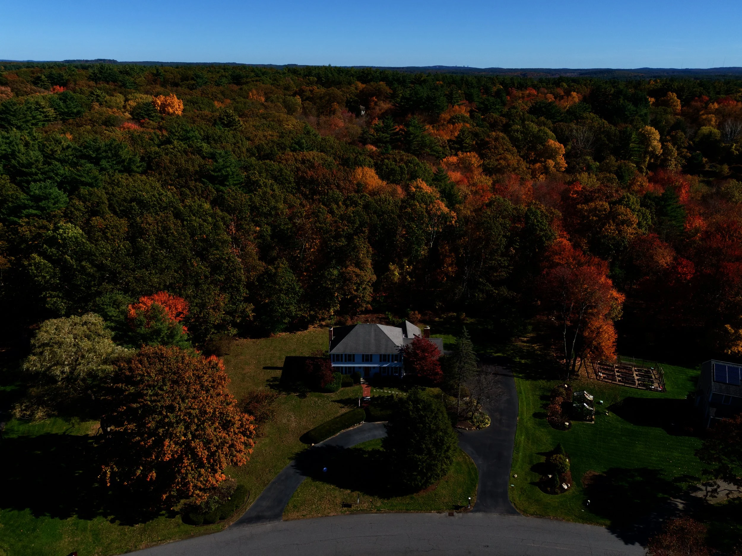 Real estate aerial, drone photography of a house in Sudbury, Massachusetts in a residential neighborhood with blue skies, a lake and foliage near Boston.