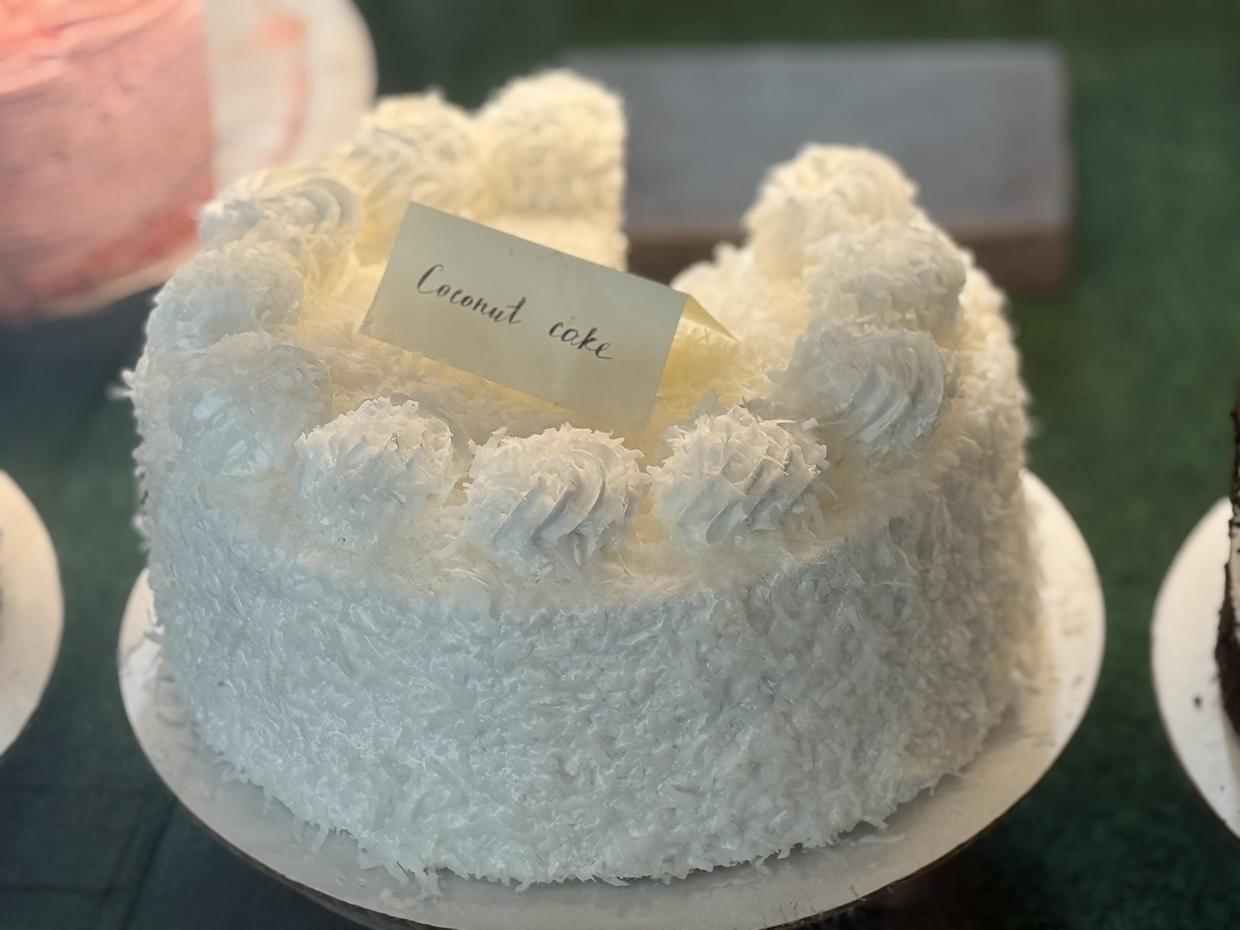 A white coconut cake decorated with coconut flakes and a small handwritten label that says 'Coconut cake.'