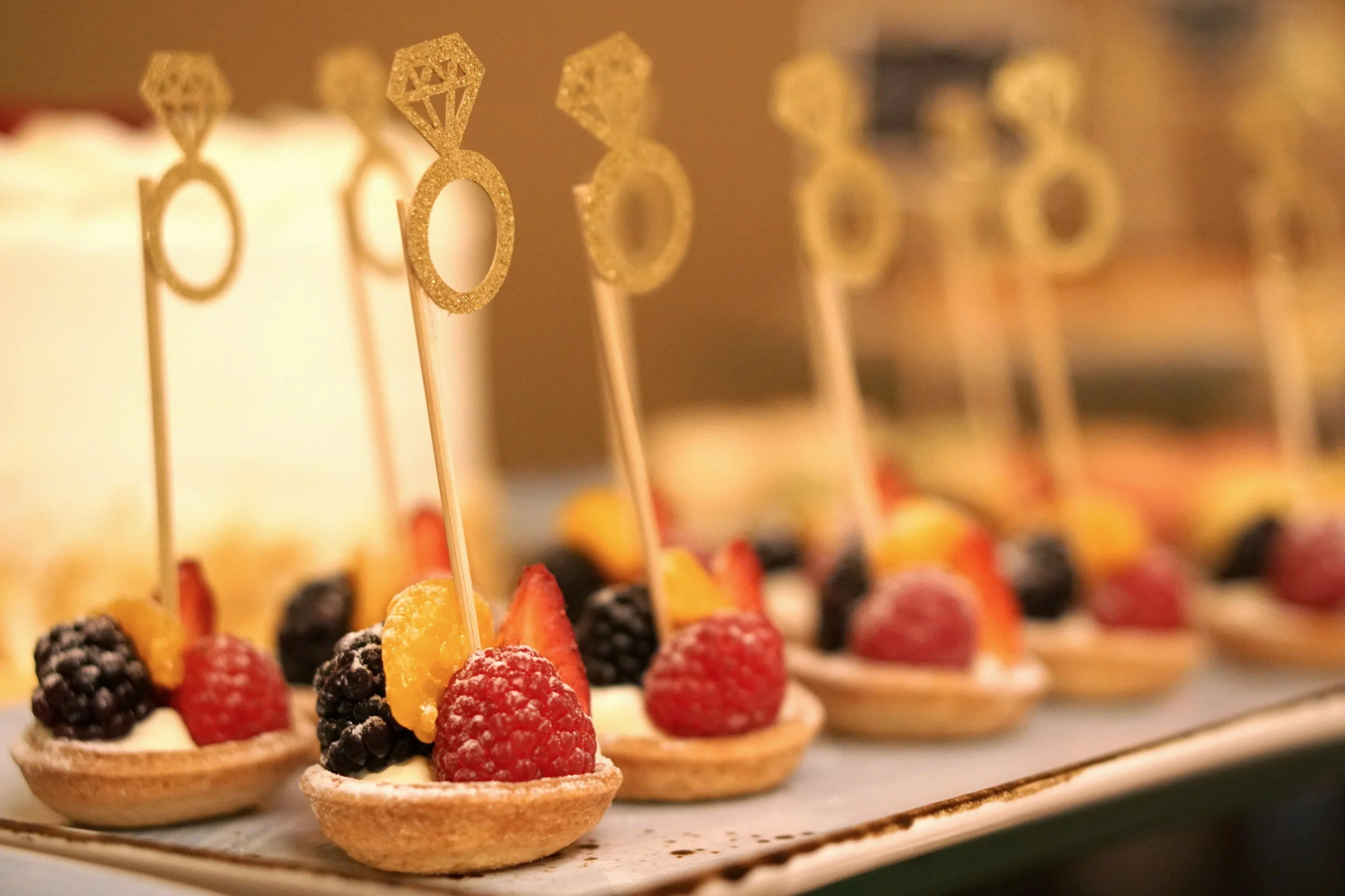 Mini fruit tartlets with assorted berries and decorative gold rings on toothpicks.