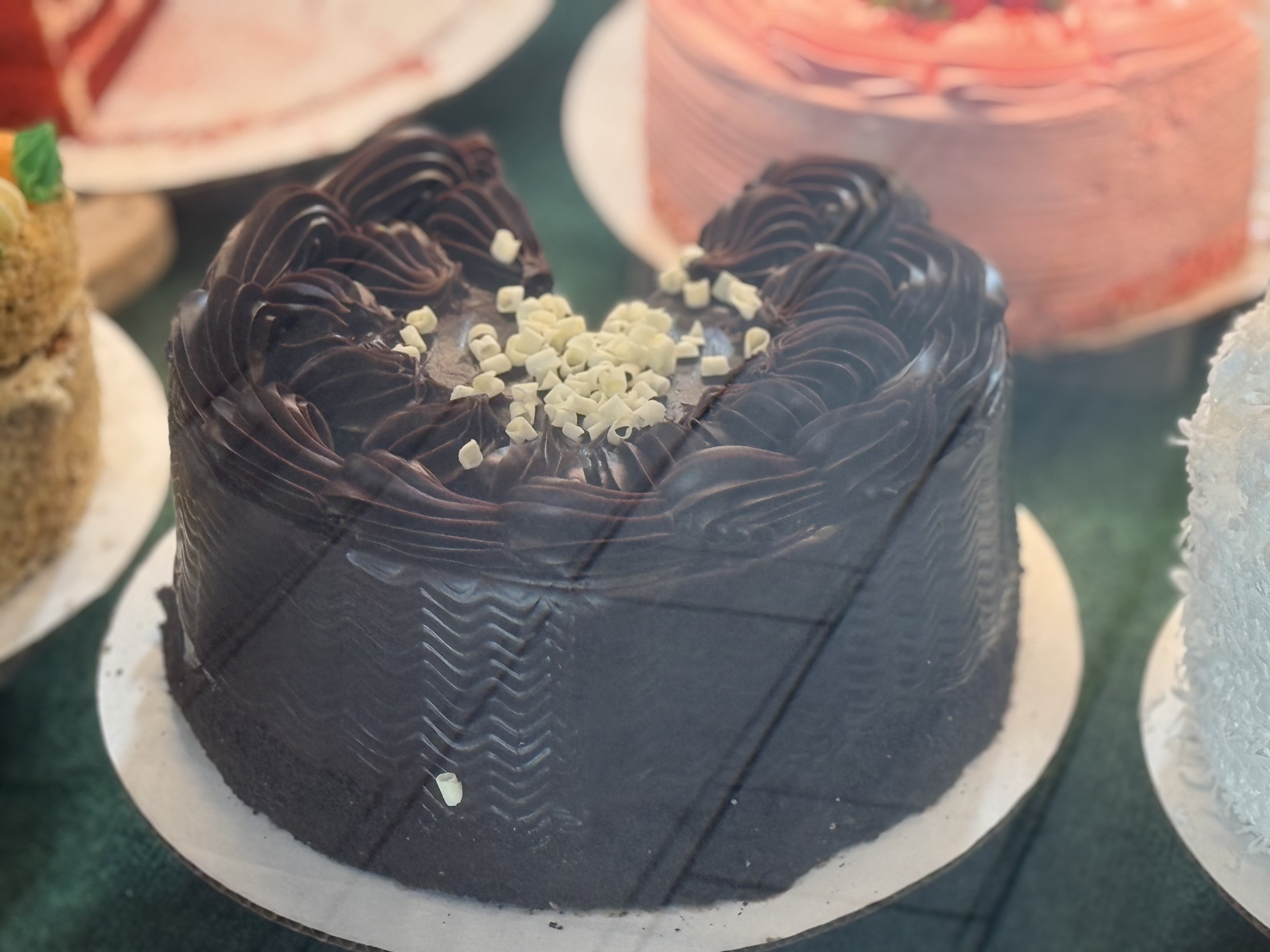A heart-shaped chocolate cake decorated with dark chocolate ganache and white chocolate shavings on top.