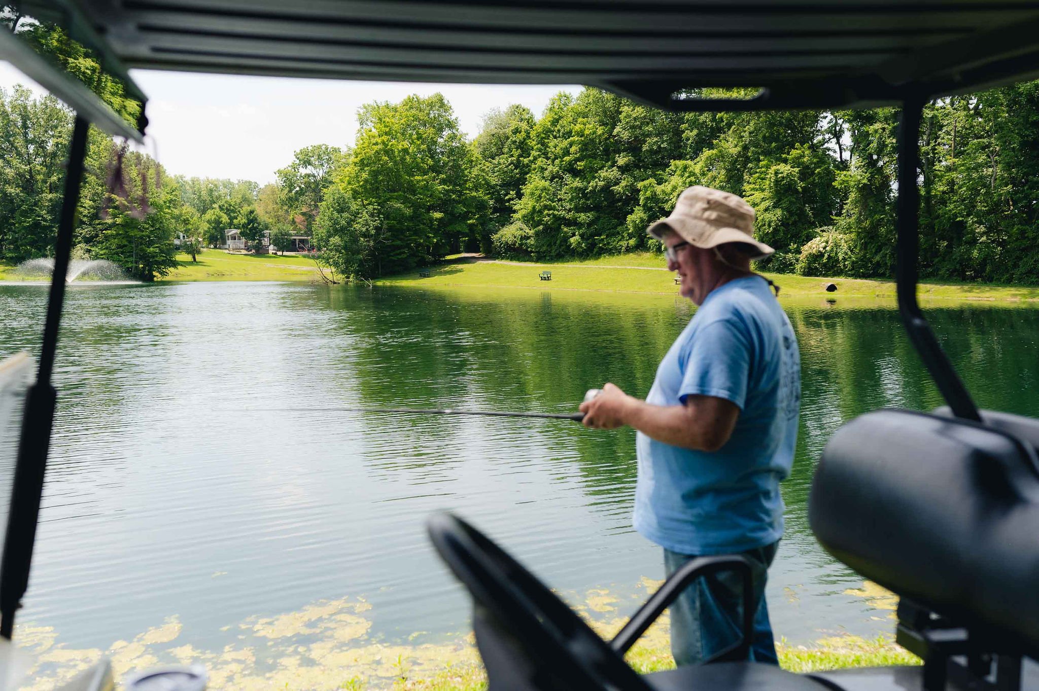 Man fishing on a lake, viewed from inside a boat, with trees and houses in the background.