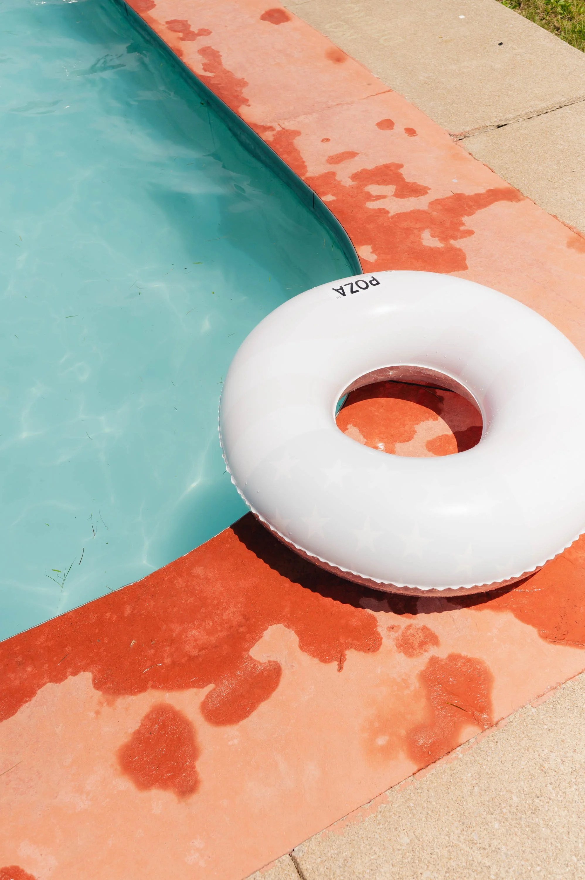 Inflatable pool float with the word 'POZA' next to a swimming pool with water and a red concrete pool deck.