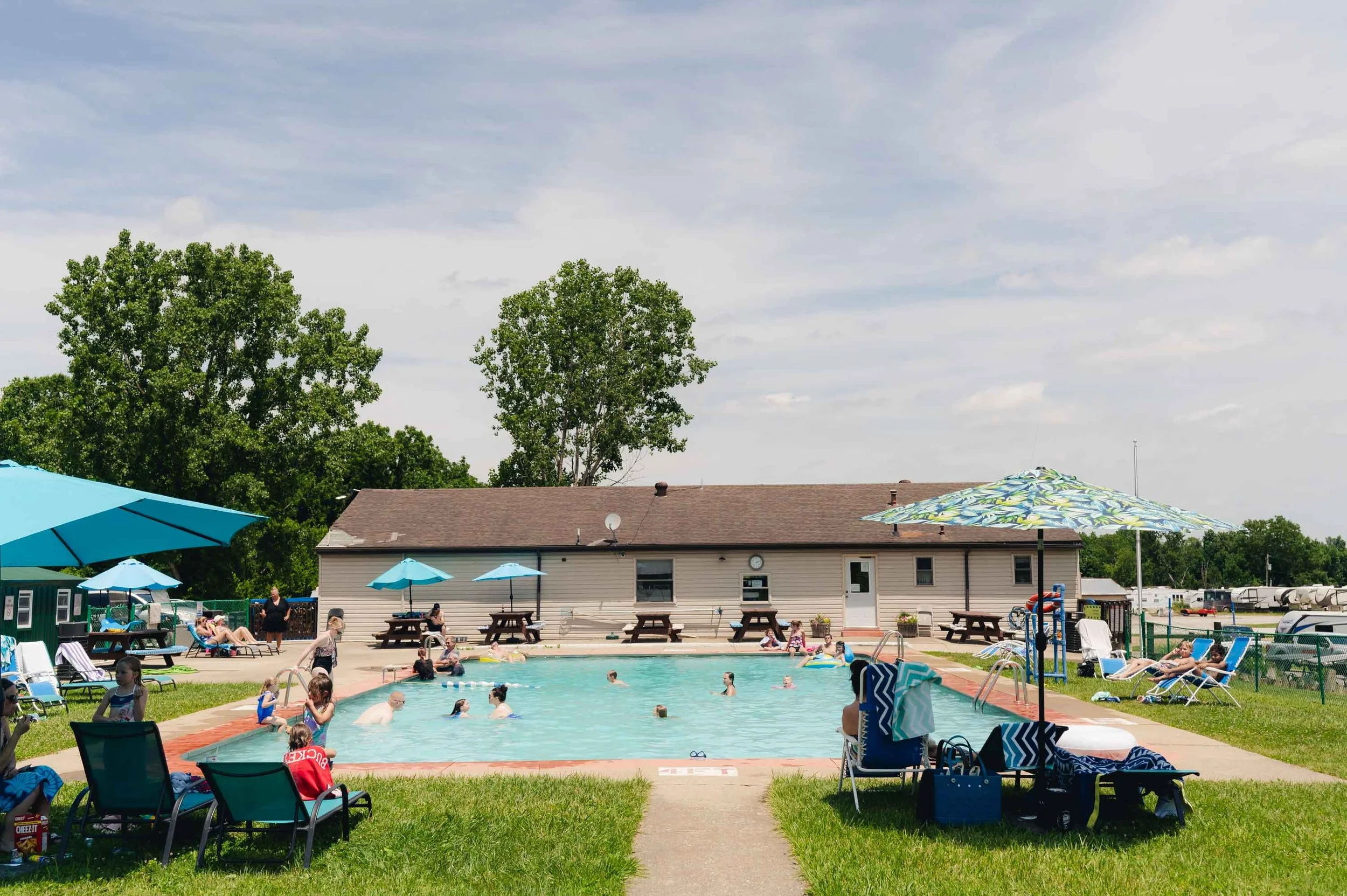 People swimming and relaxing around a swimming pool with umbrellas and a building in the background.