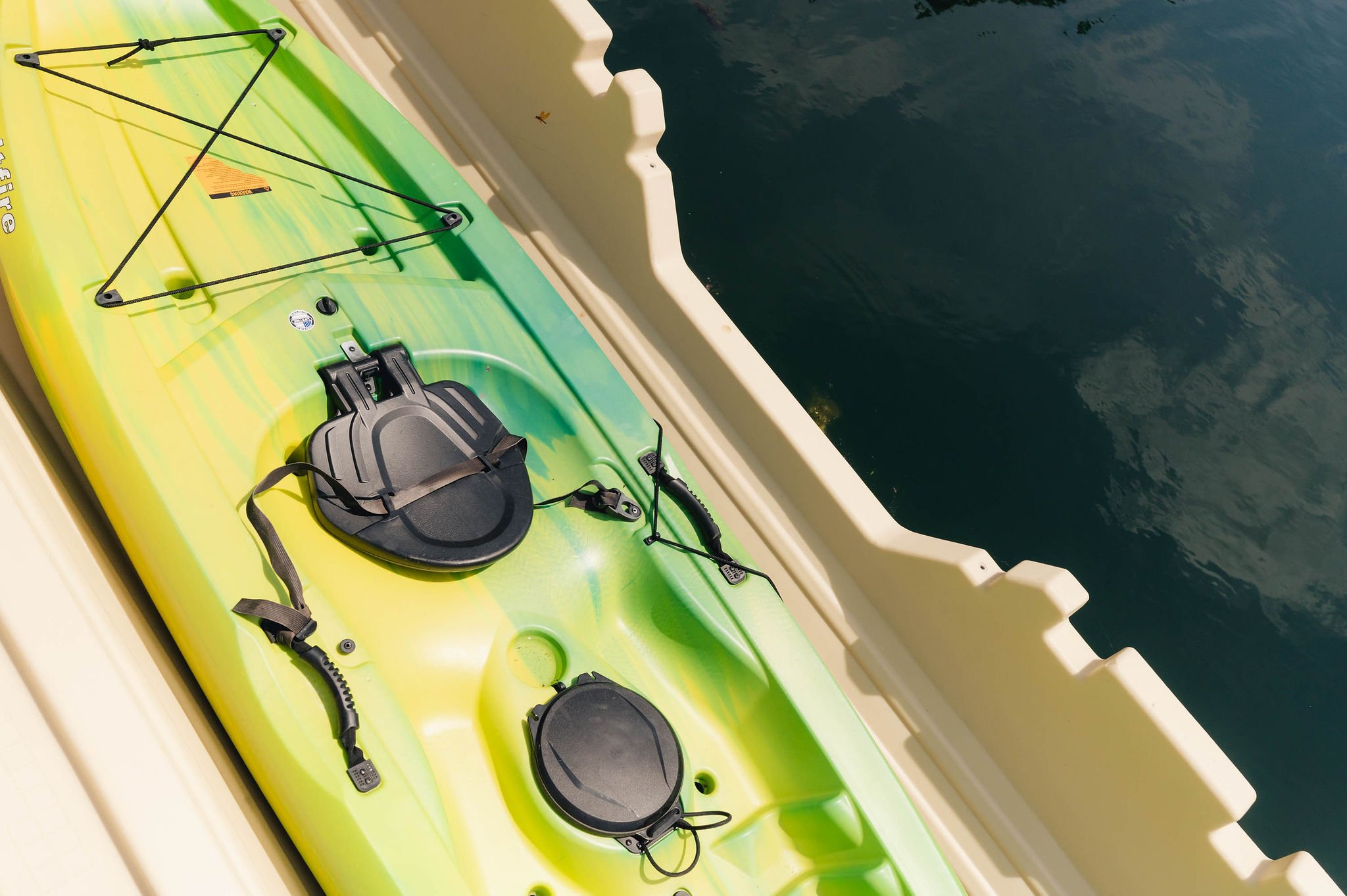 Close-up of a green kayak with black bungee cords and two round hatches, on a boat near dark water.