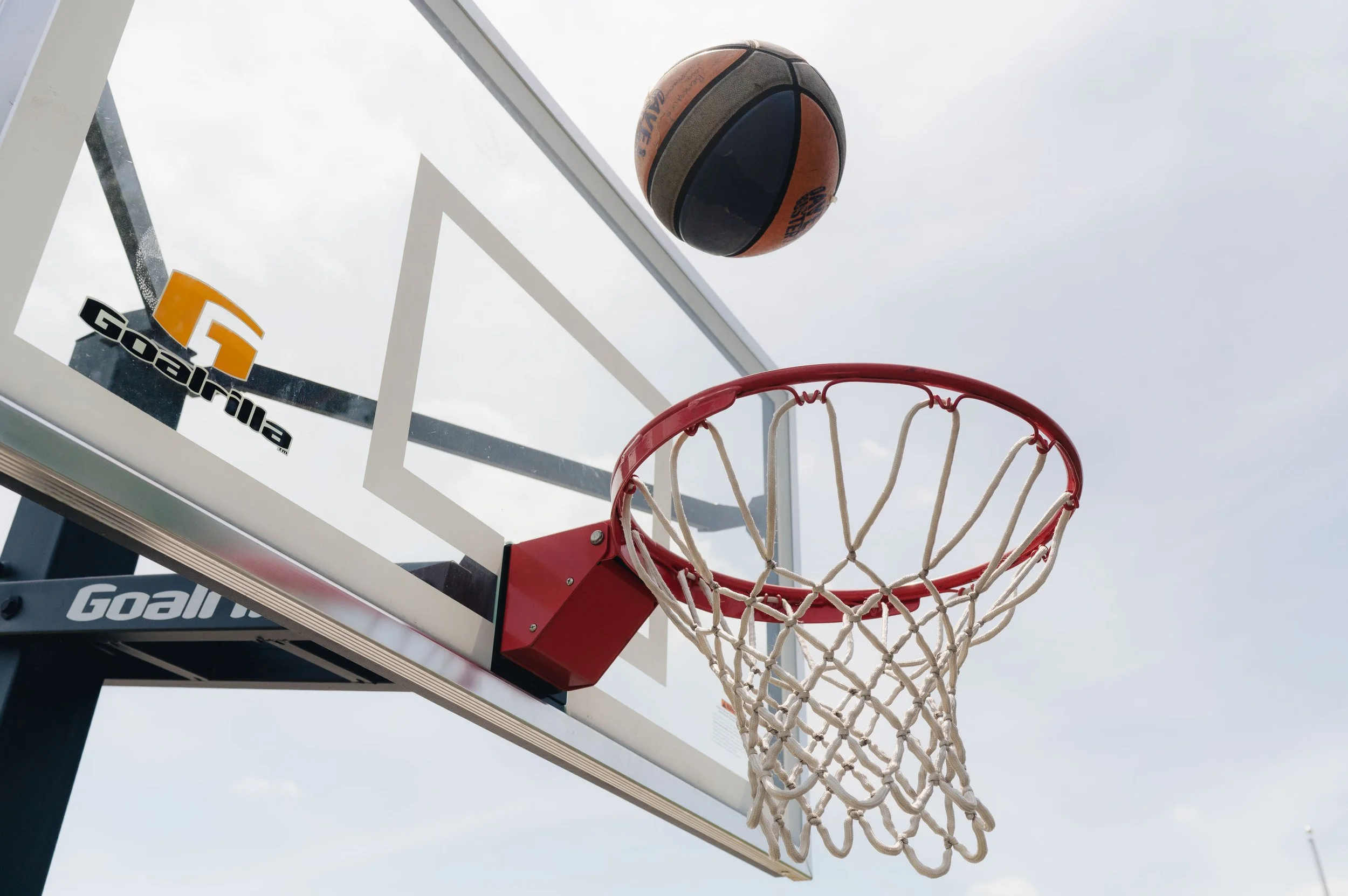 Basketball hoop with a basketball flying towards the hoop against a cloudy sky.