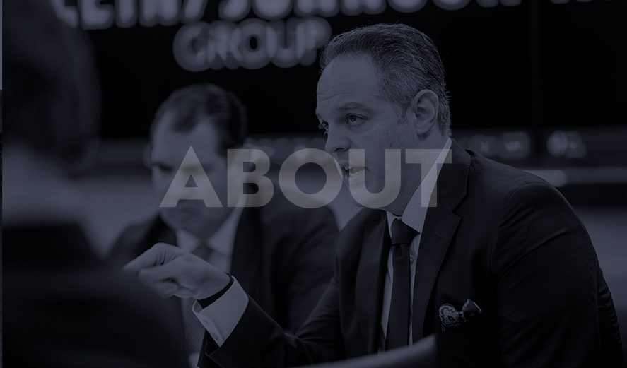 Two men in suits engaged in a serious conversation in a professional setting with the word "About" overlaid on the image.