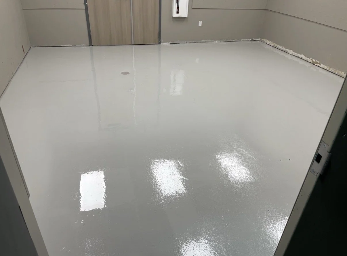 Empty garage with unfinished drywall walls, two small windows, and a concrete floor.