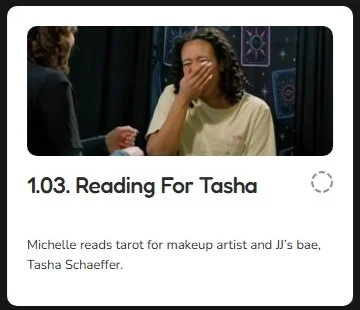 A woman covering her face with her hand while sitting at a table with another person, with a backdrop of celestial designs.
