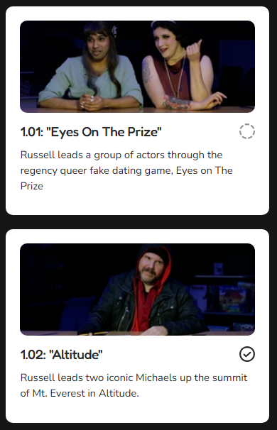 Two women sitting at a table, smiling, with one resting her arm on the table and the other touching her chin, and a man sitting at a desk wearing a red hoodie and black jacket, in a studio setting.