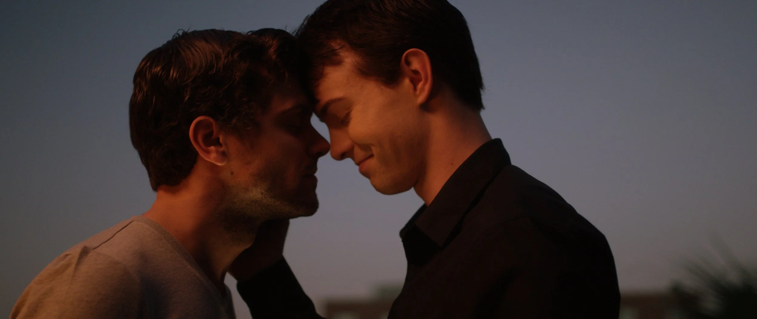 Two men gently pressing foreheads together at sunset, creating an intimate moment.
