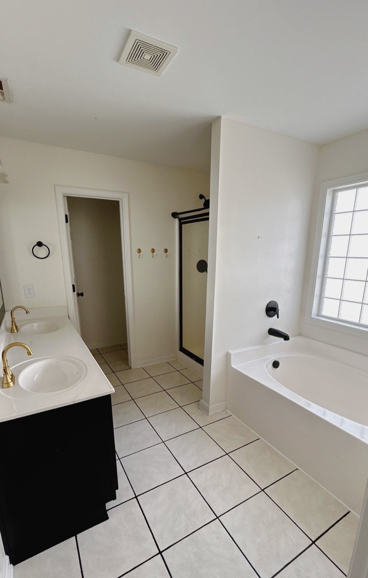 Modern bathroom with double sink vanity, gold fixtures, tile flooring, glass shower, bathtub, and large window for natural light.