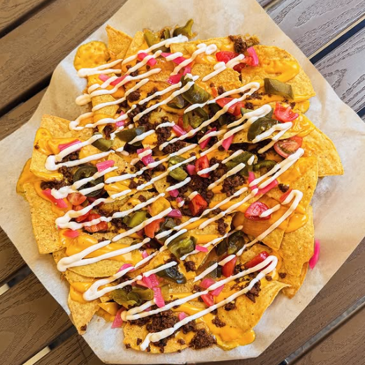 A plate of nachos topped with melted cheese, diced tomatoes, jalapeños, sour cream, and other toppings.