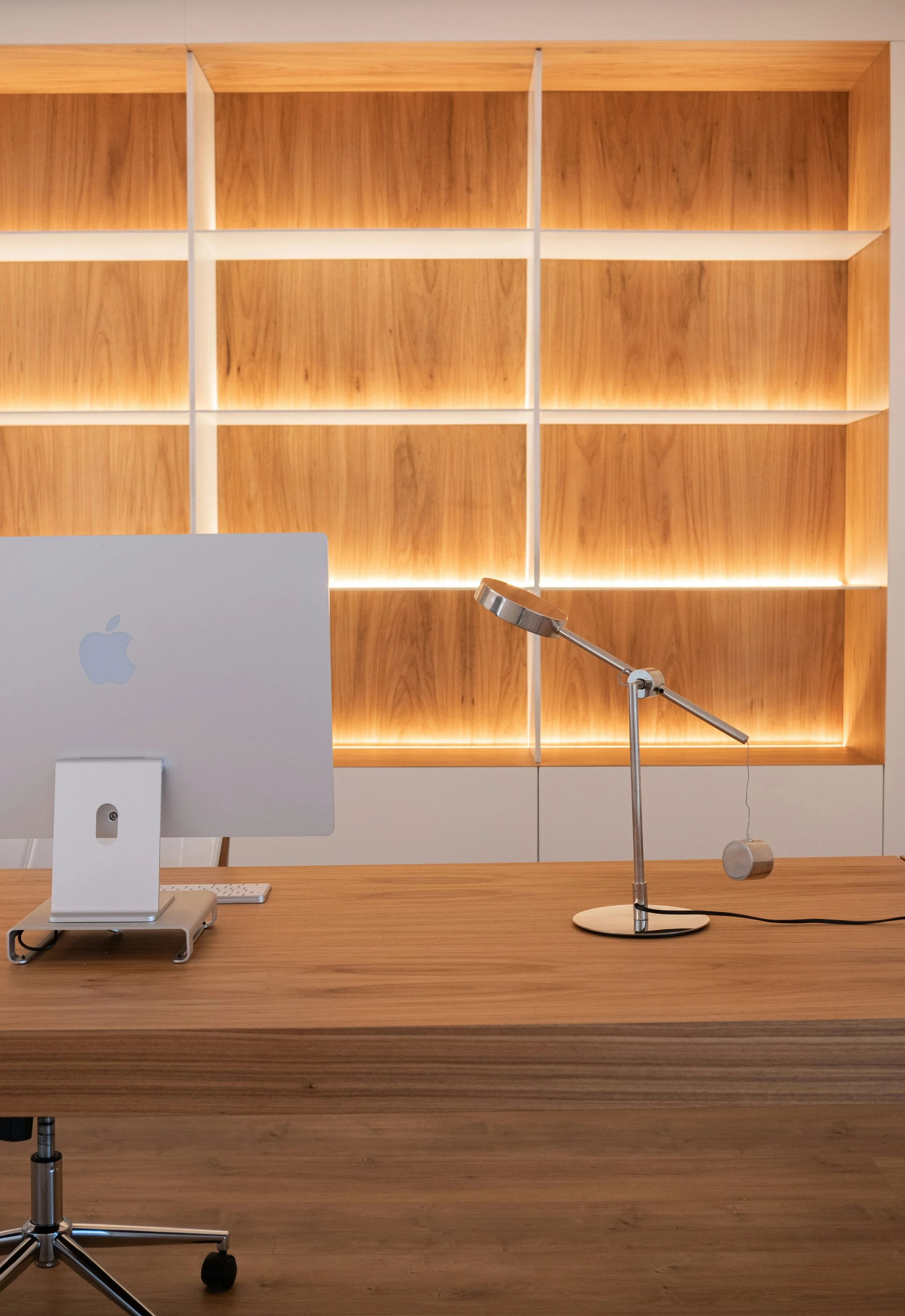 Bureau moderne avec un ordinateur Apple, une lampe de bureau en métal, et une étagère en bois éclairée par des lumières intégrées.