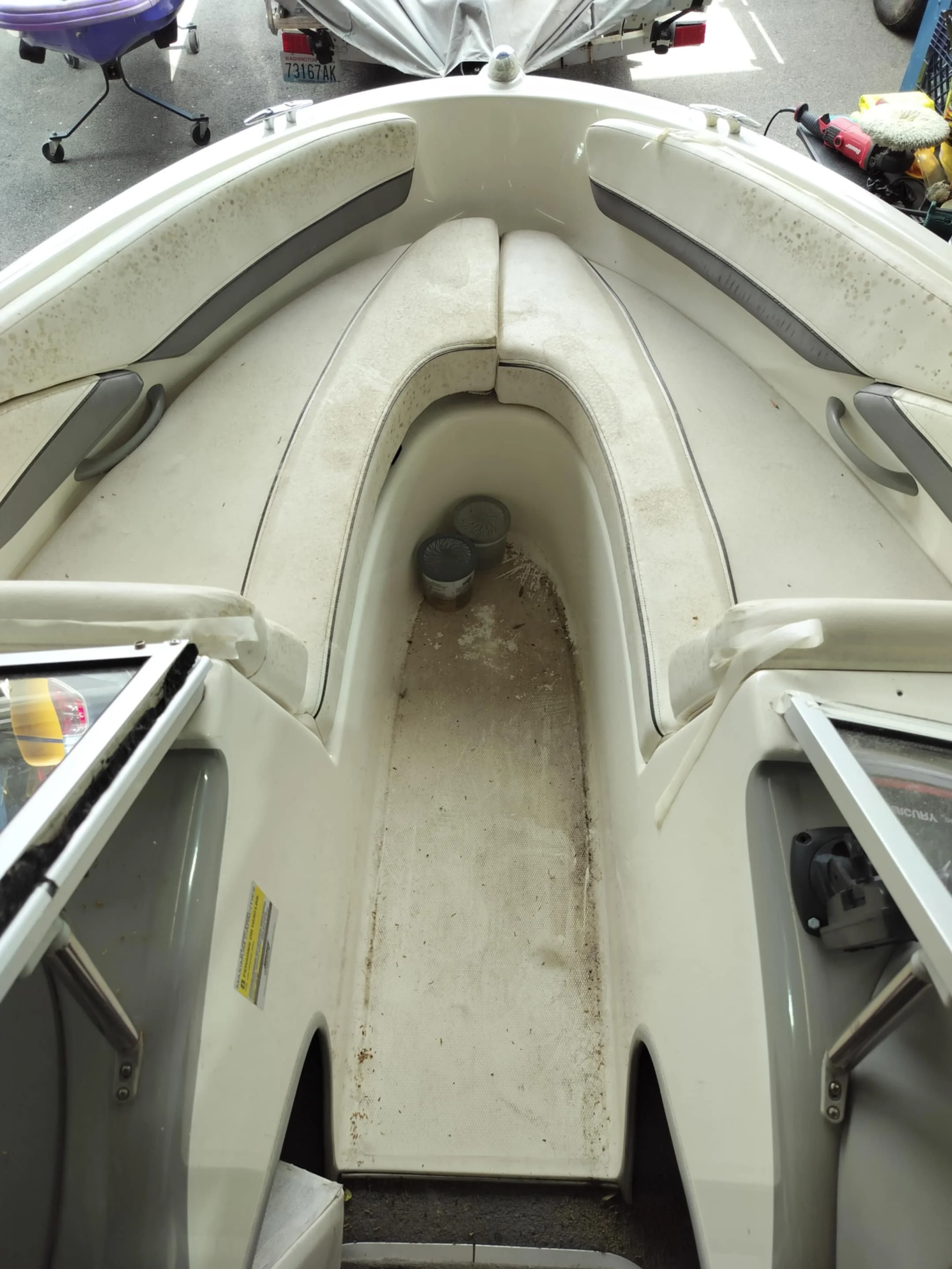 Inside of an empty, dirty boat with built-in seating and two small containers on the floor.