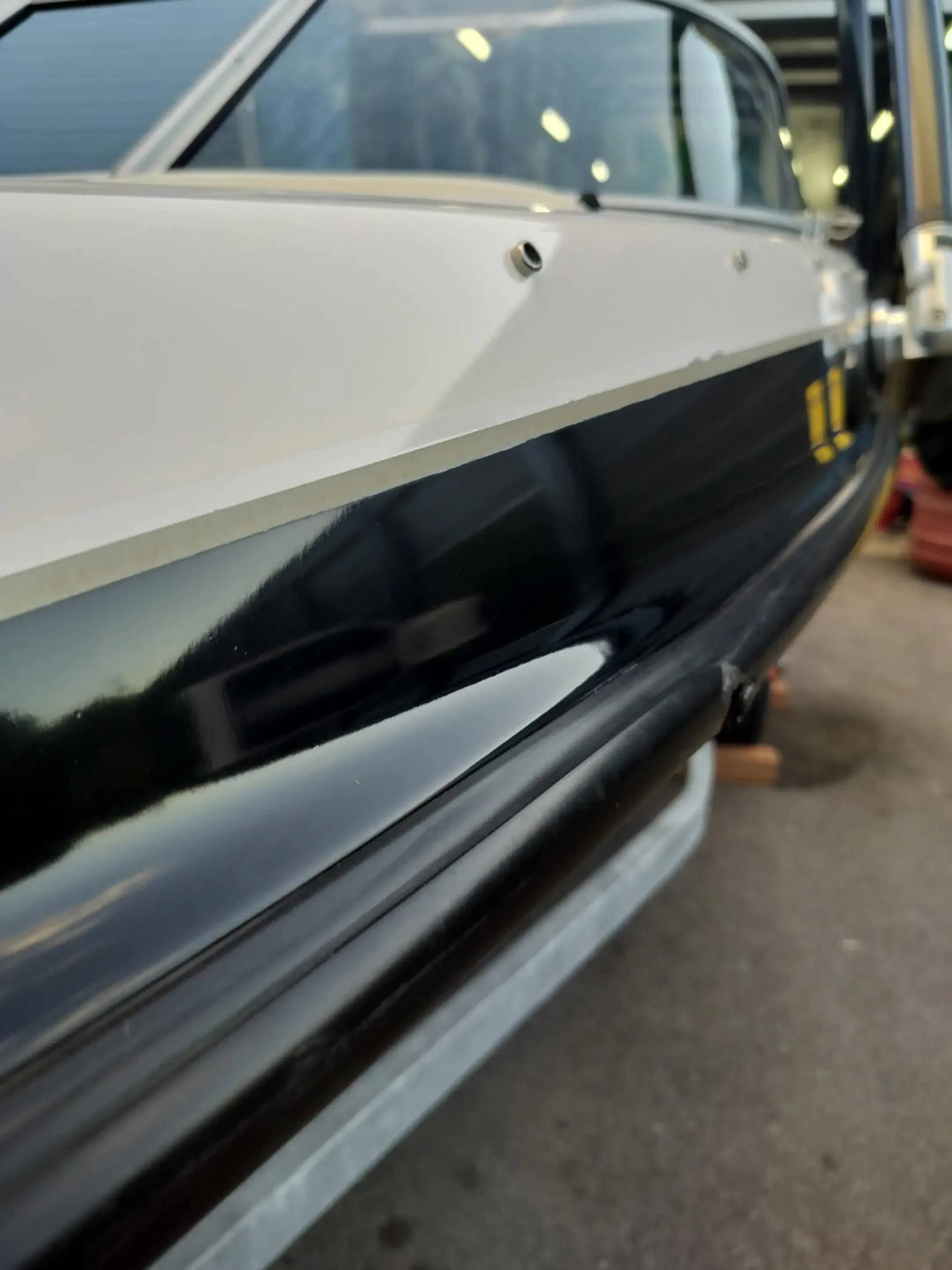 Close-up of a vintage black and white car in a garage or workshop, with parts of the vehicle missing or under repair.