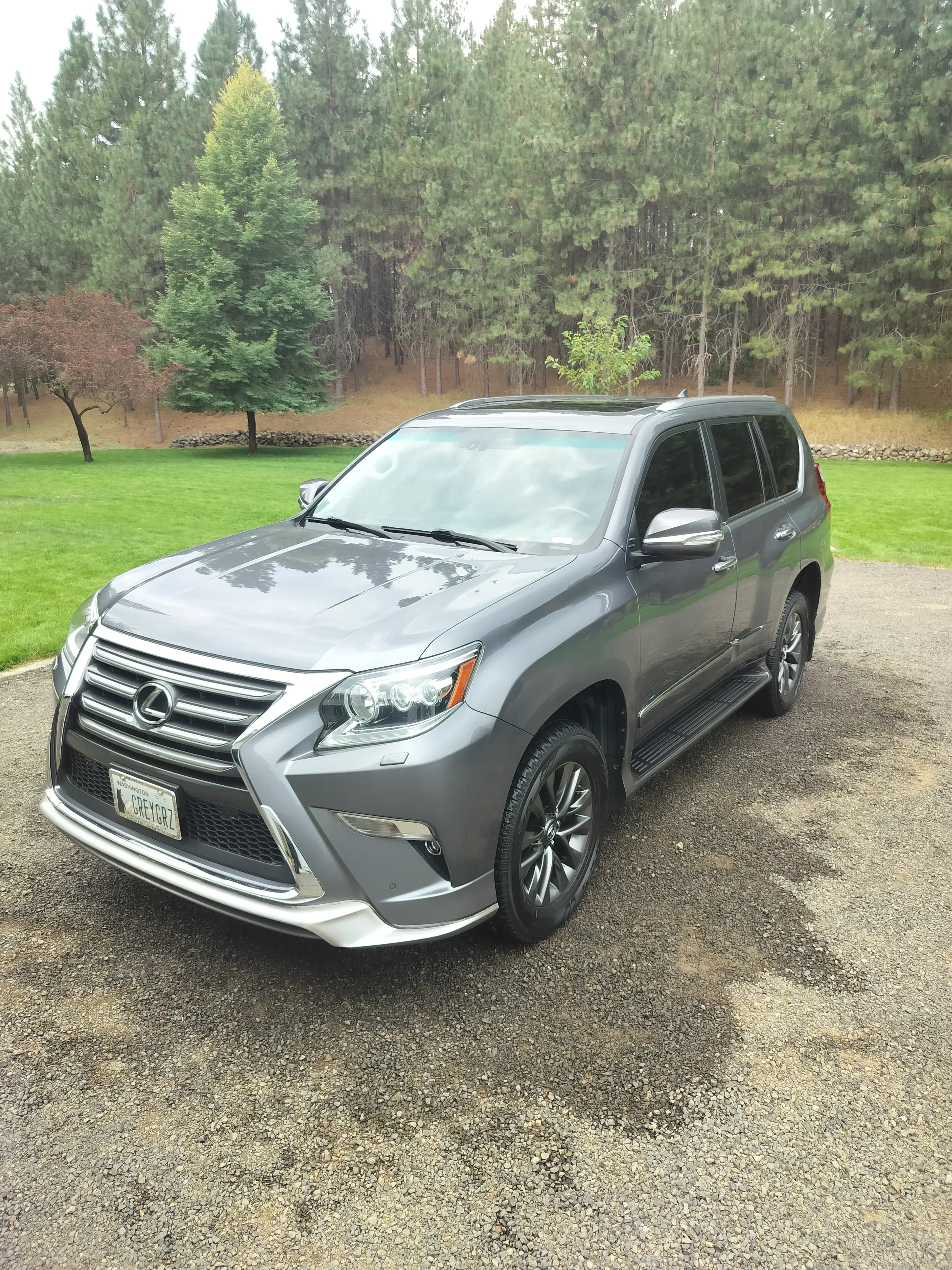 A silver Lexus SUV parked on a gravel driveway with a green lawn and trees in the background.
