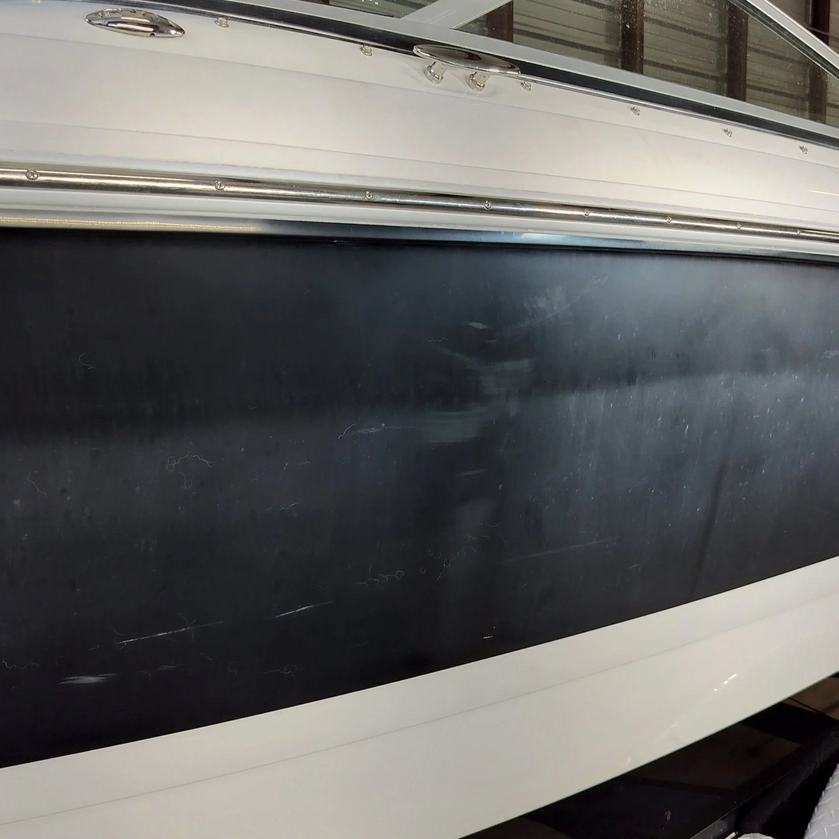 Close-up of a black surface with scratches, part of a boat with a white and silver exterior, showing metal railings and windows.
