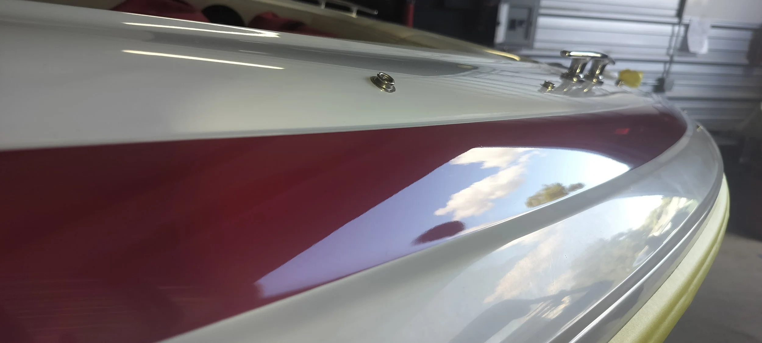 Close-up of a red and white boat with clouds peeking through on the reflection of its high gloss finish