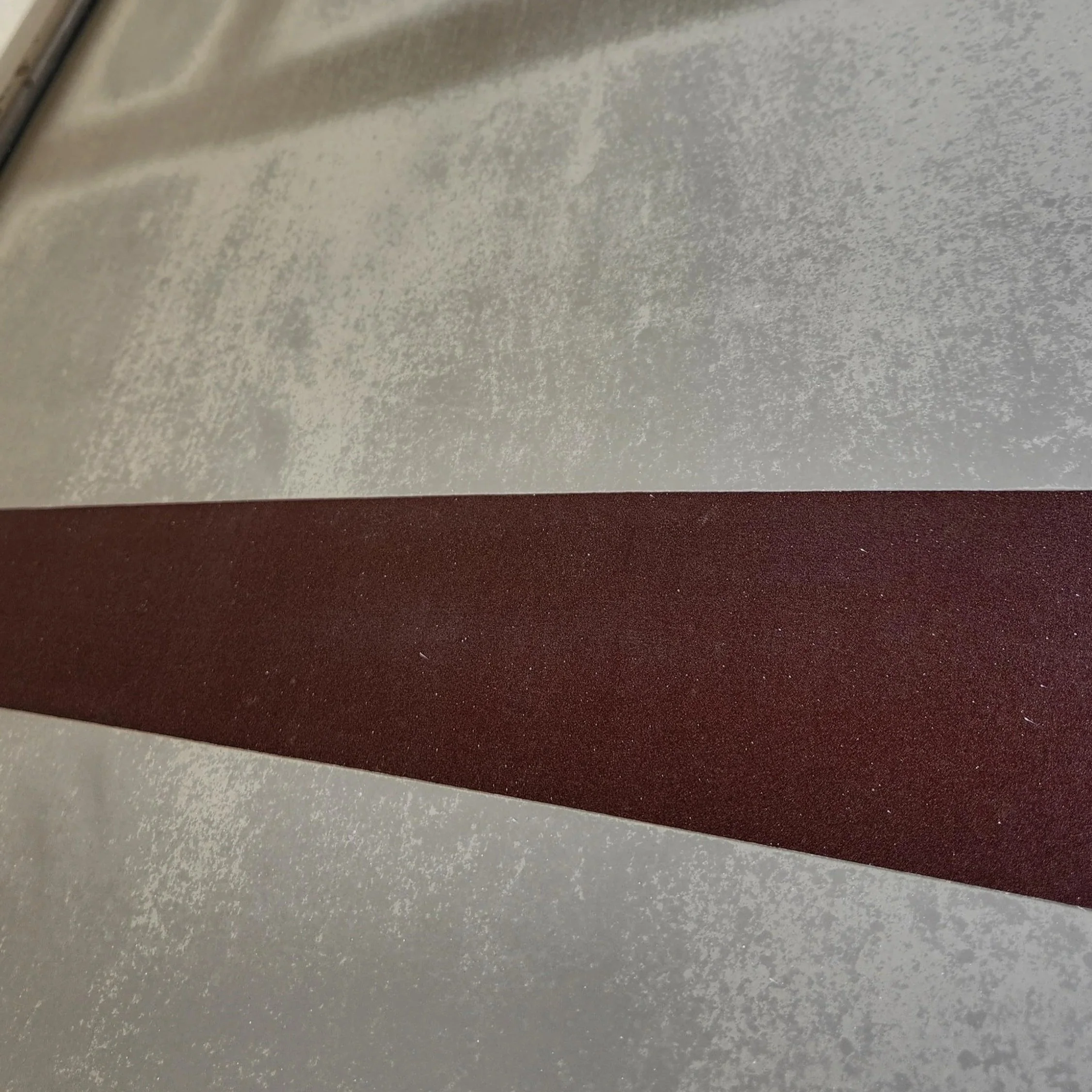 Close-up of a metallic surface with a horizontal maroon stripe.