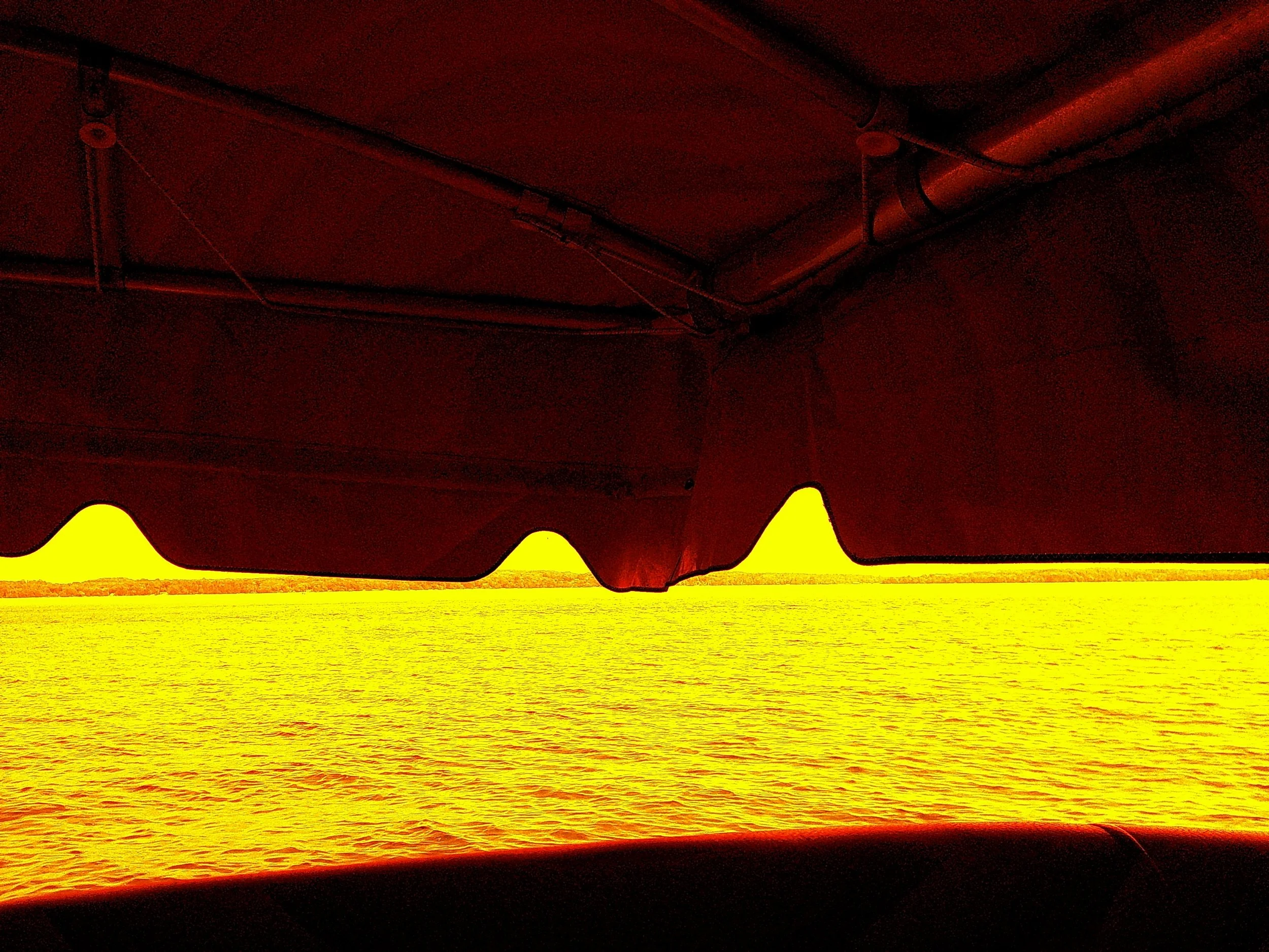 View of the water and distant shoreline through a boat's canopy with the sun setting, casting a yellow and red glow.
