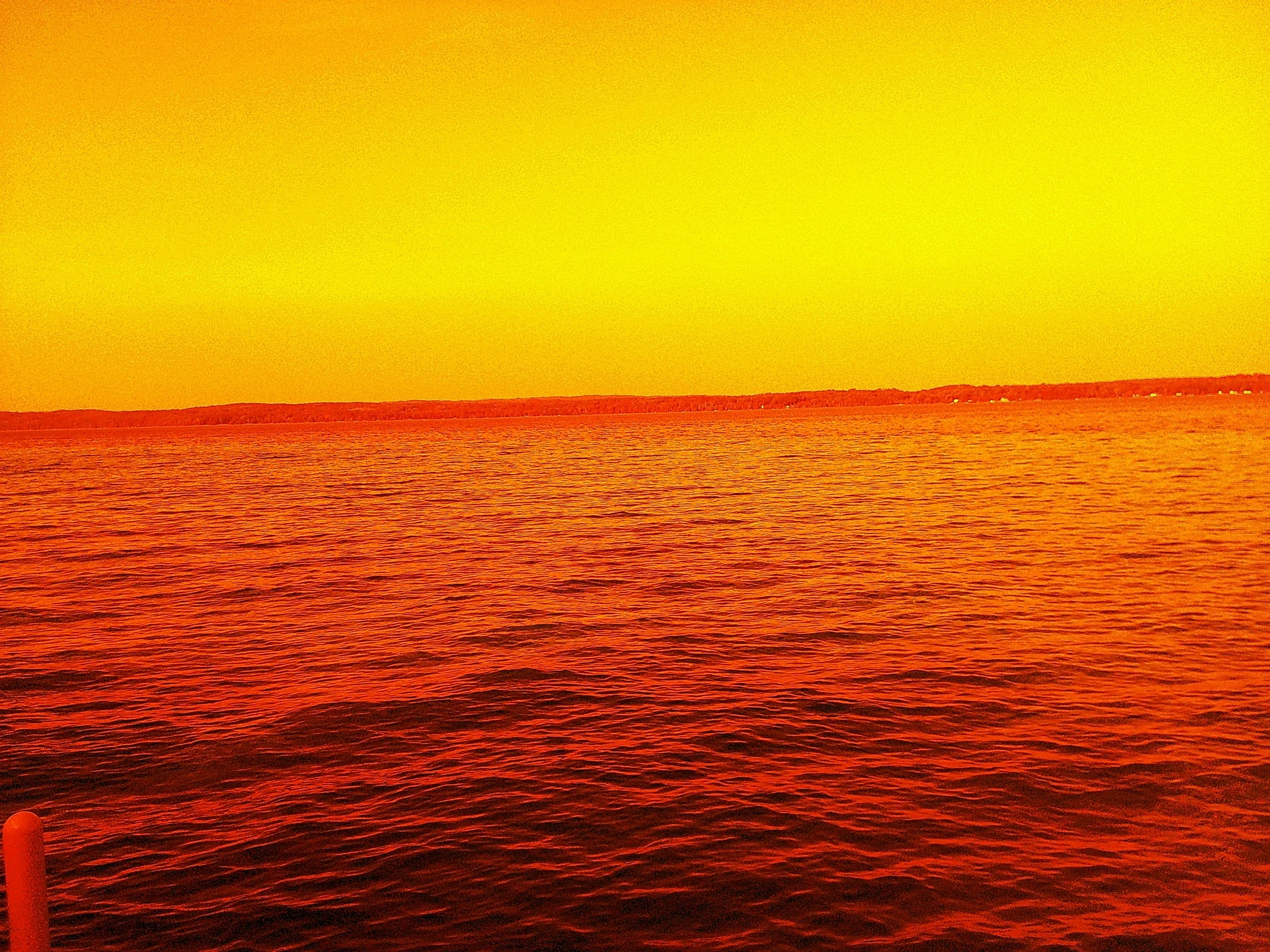 Sunset over a body of water with orange and red hues in the sky and rippling water surface.