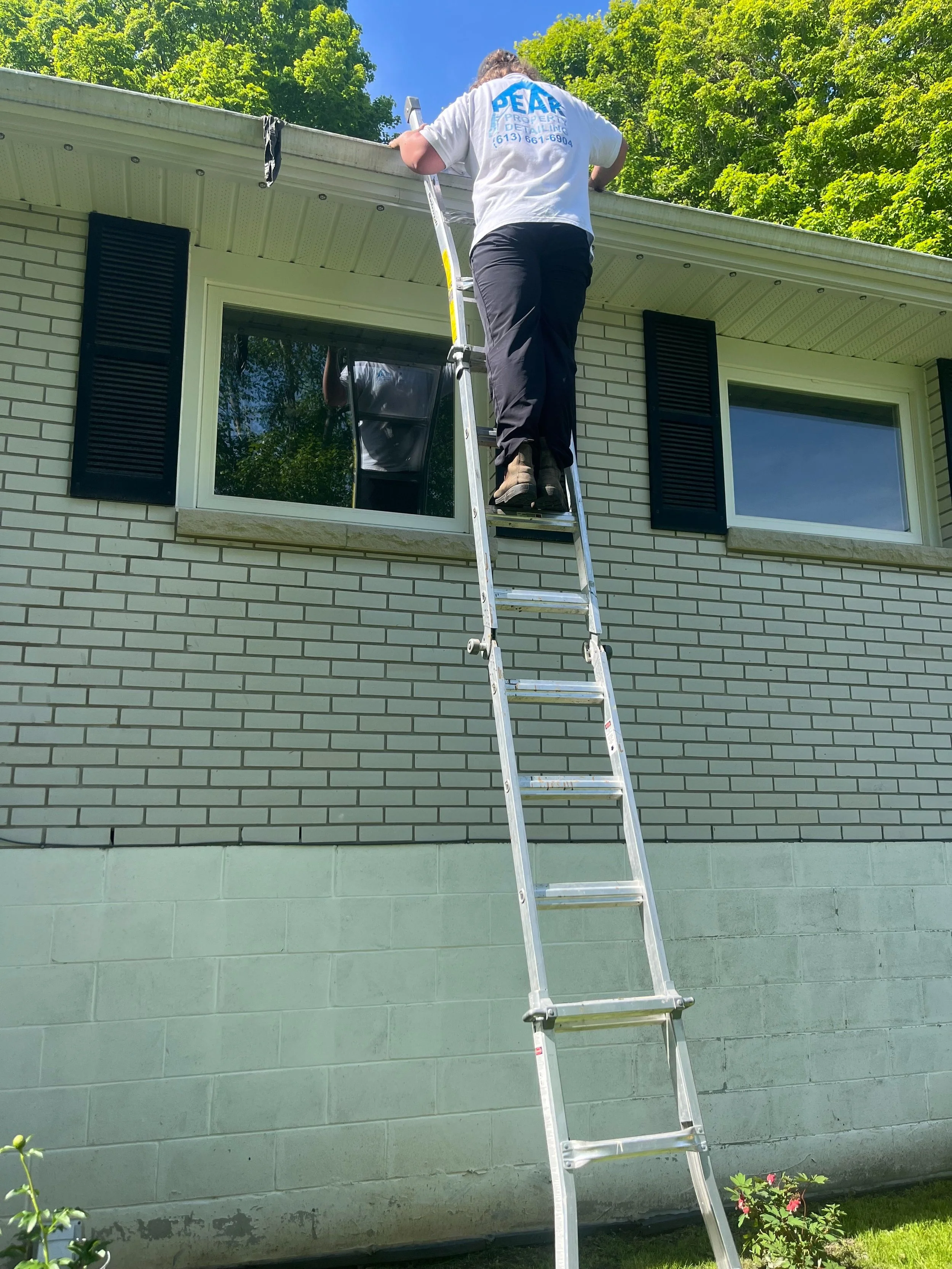 Peak Property Detailing technician cleaning residential eaves with professional equipment, removing debris and buildup to improve drainage and curb appeal. Belleville-Trenton-Frankford-