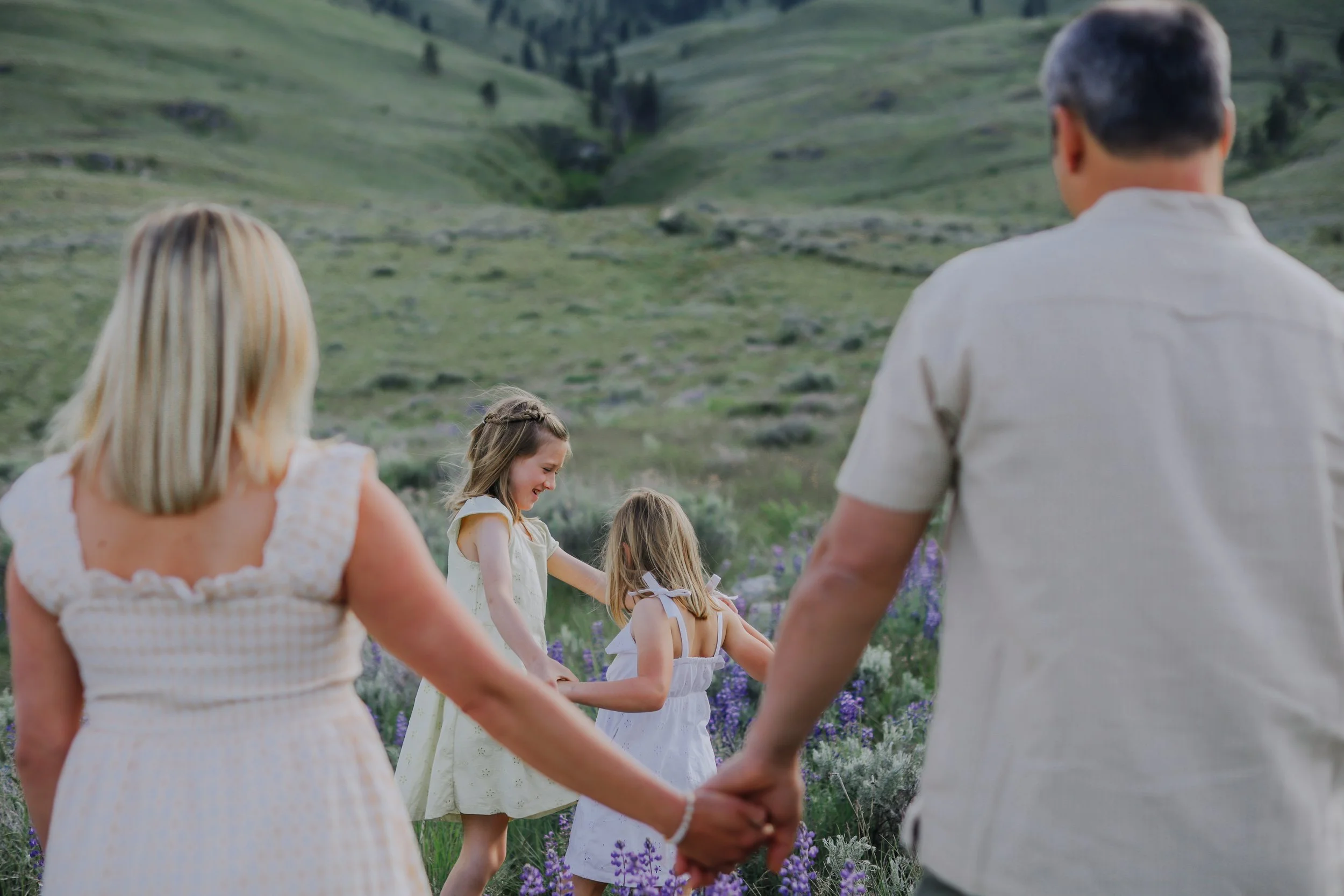 A group of people holding hands and forming a circle in a field of purple flowers with green hills in the background