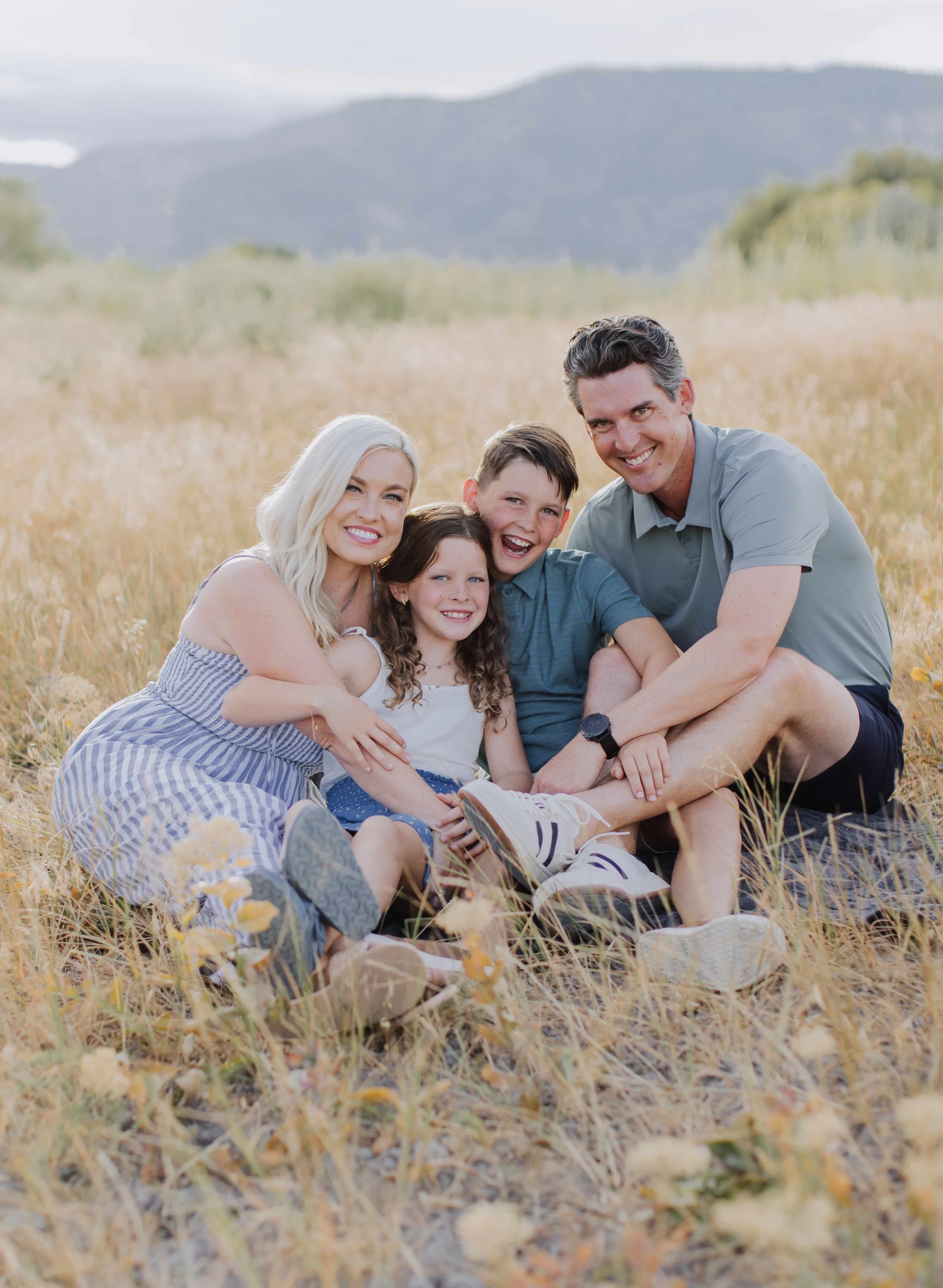 FAMILY WITH 2 ELEMENTARY AGED KIDS SMILING IN A FEILD OF WHEAT GRASS