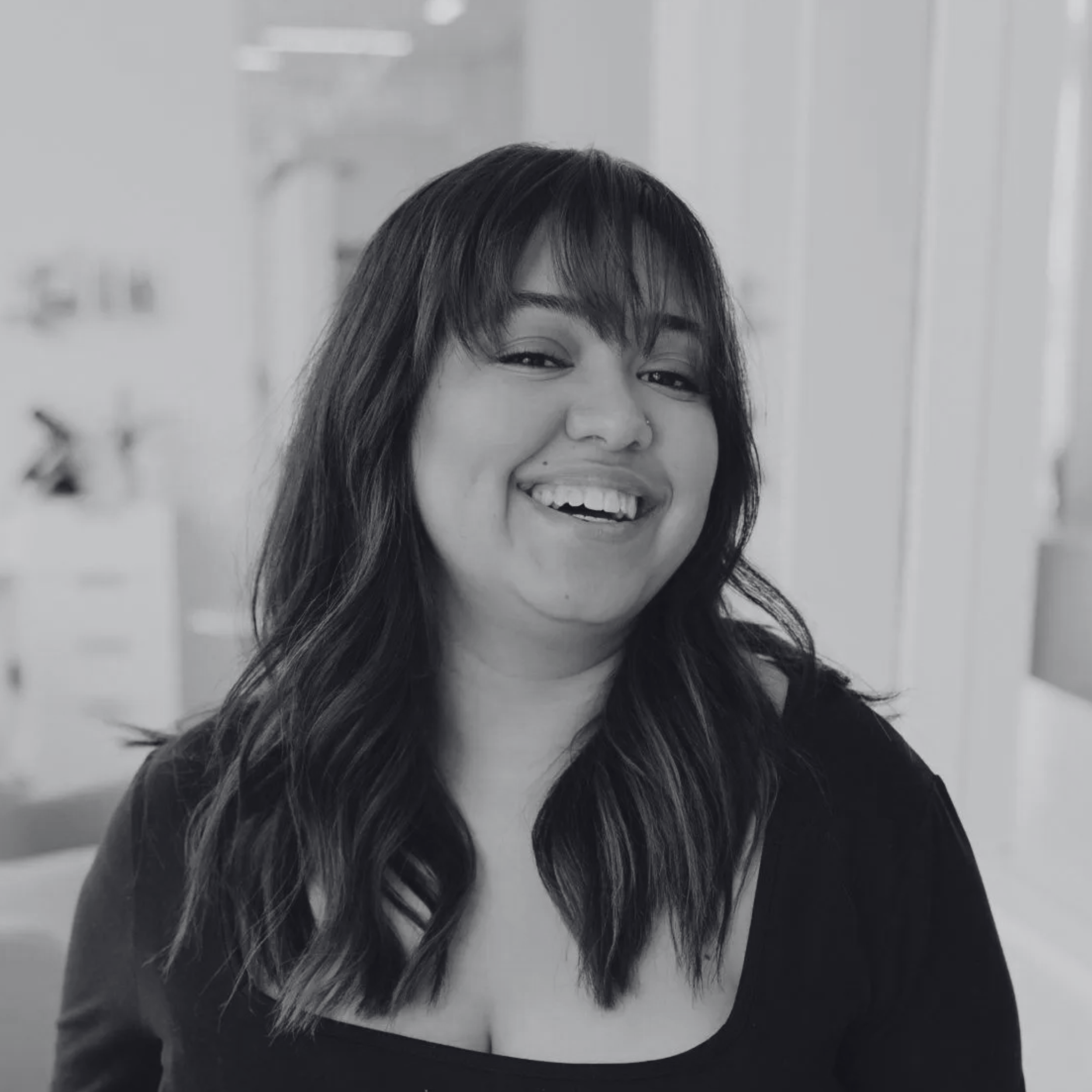 Black and white photo of a woman with shoulder-length wavy hair and bangs, smiling.