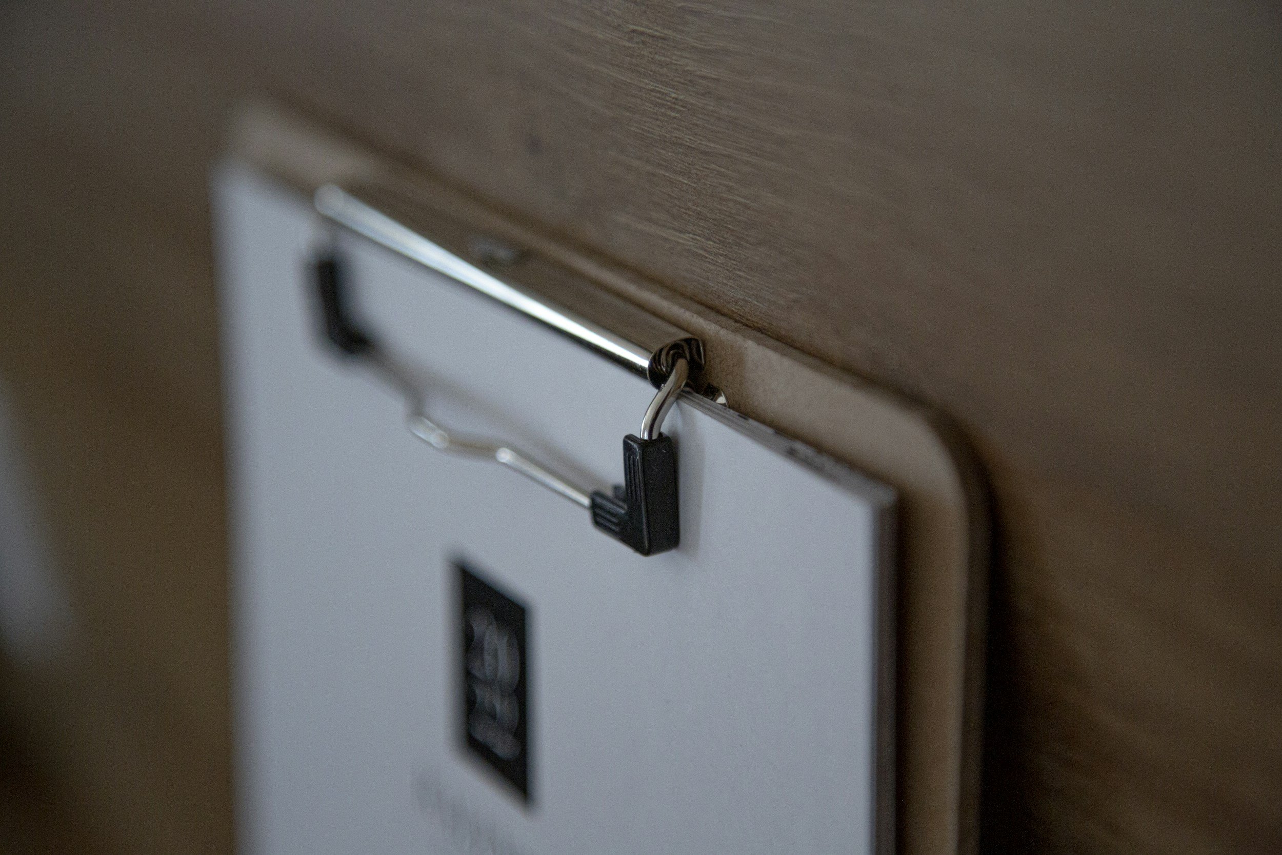 A close-up of a metal clip on a white paper with black text attached to a wooden surface.
