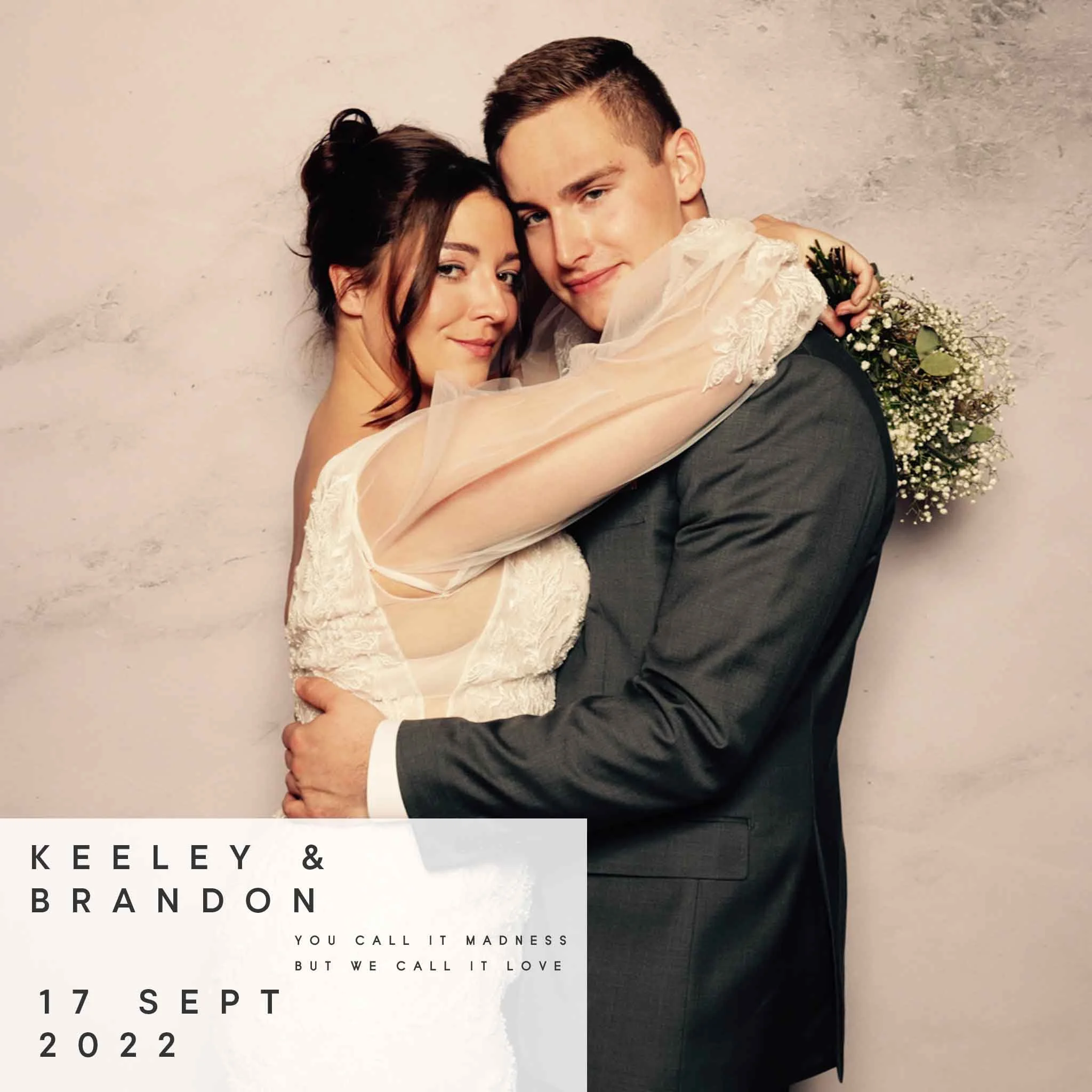 A bride and groom in a wedding embrace, standing against a neutral background. The bride holds a bouquet of white flowers and wears a lace wedding dress with sheer sleeves. The groom is dressed in a dark suit. Text on the image reads: "Keeley & Brand
