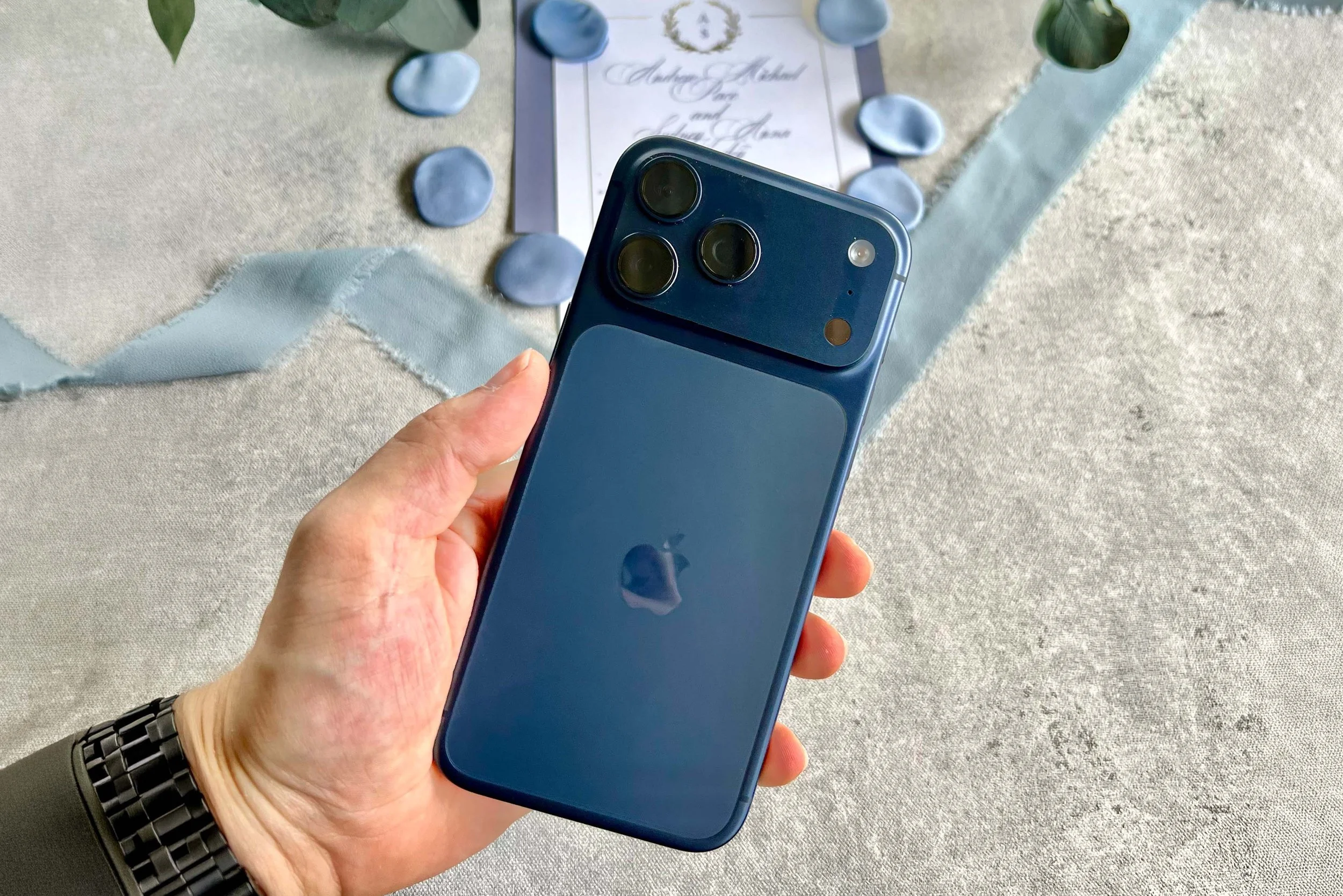 hand holding iPhone with wedding flat lay details