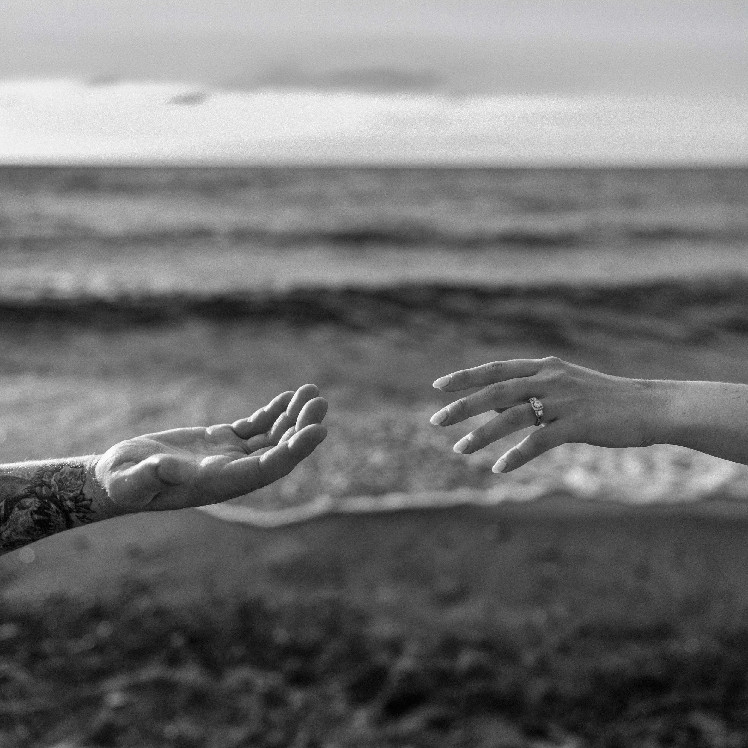 Close-up of two hands reaching towards each other with a blurred ocean background.