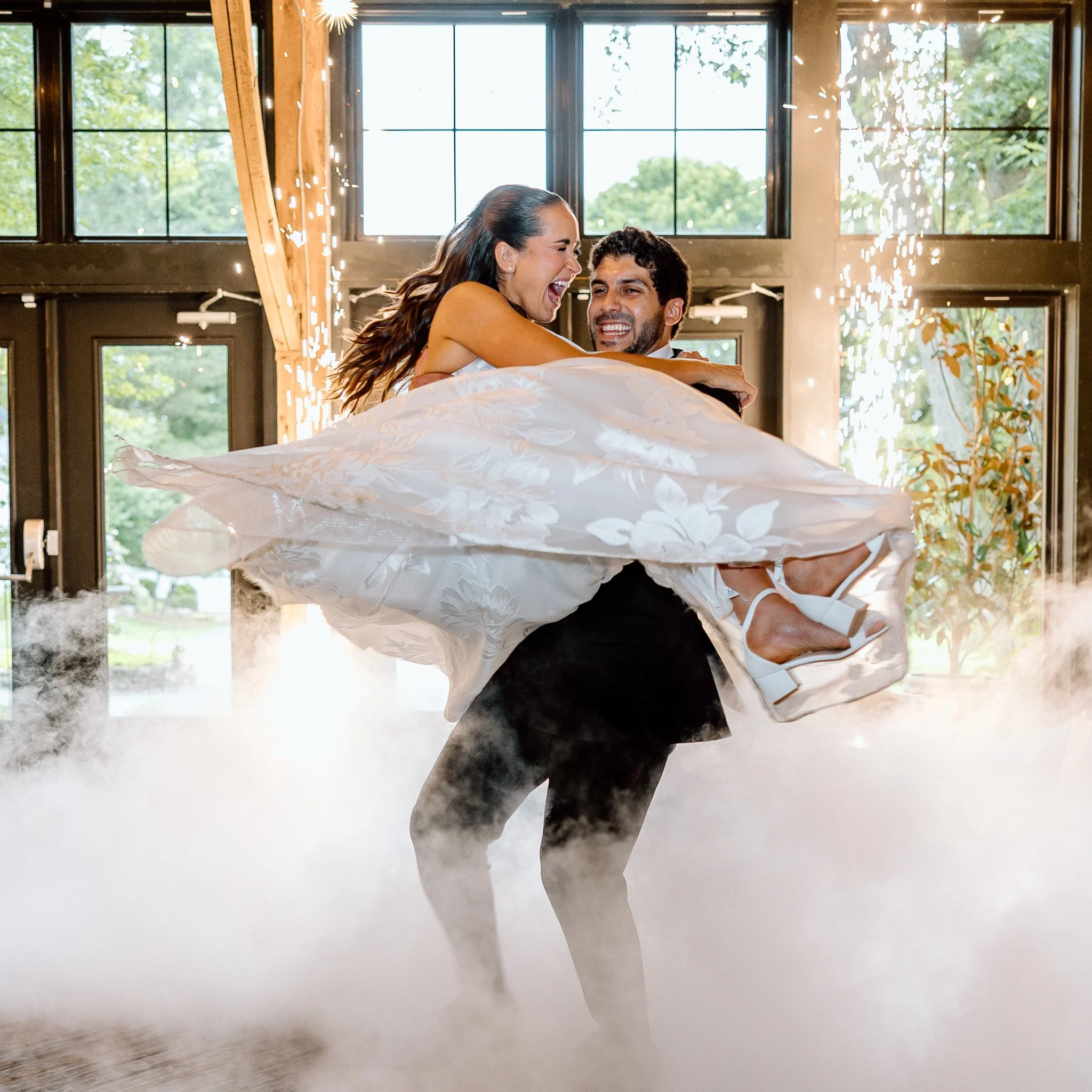 Couple dancing indoors with large windows in the background, lights, and natural scenery outside.