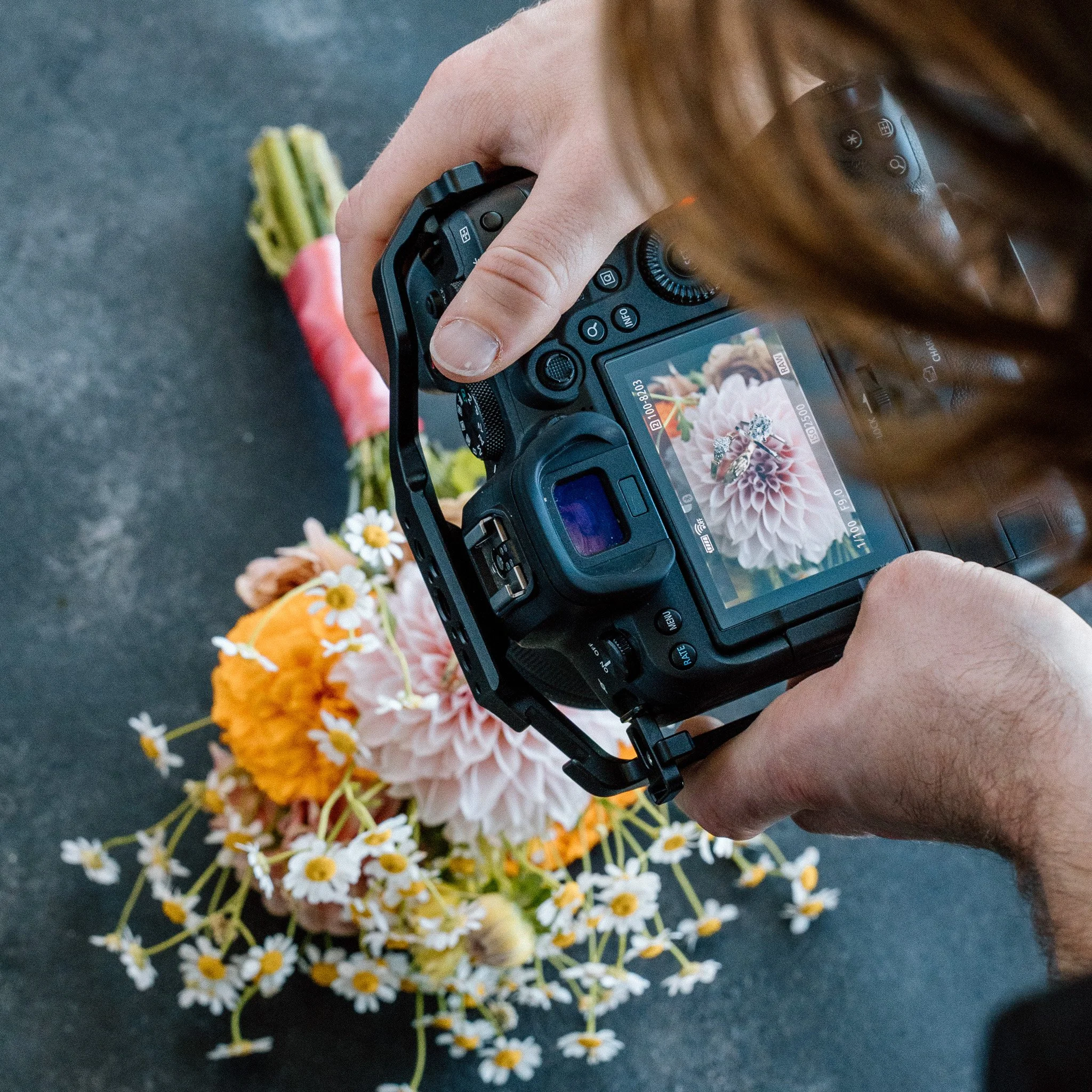 A person using a camera to photograph a bunch of small white and yellow daisies on a dark surface.