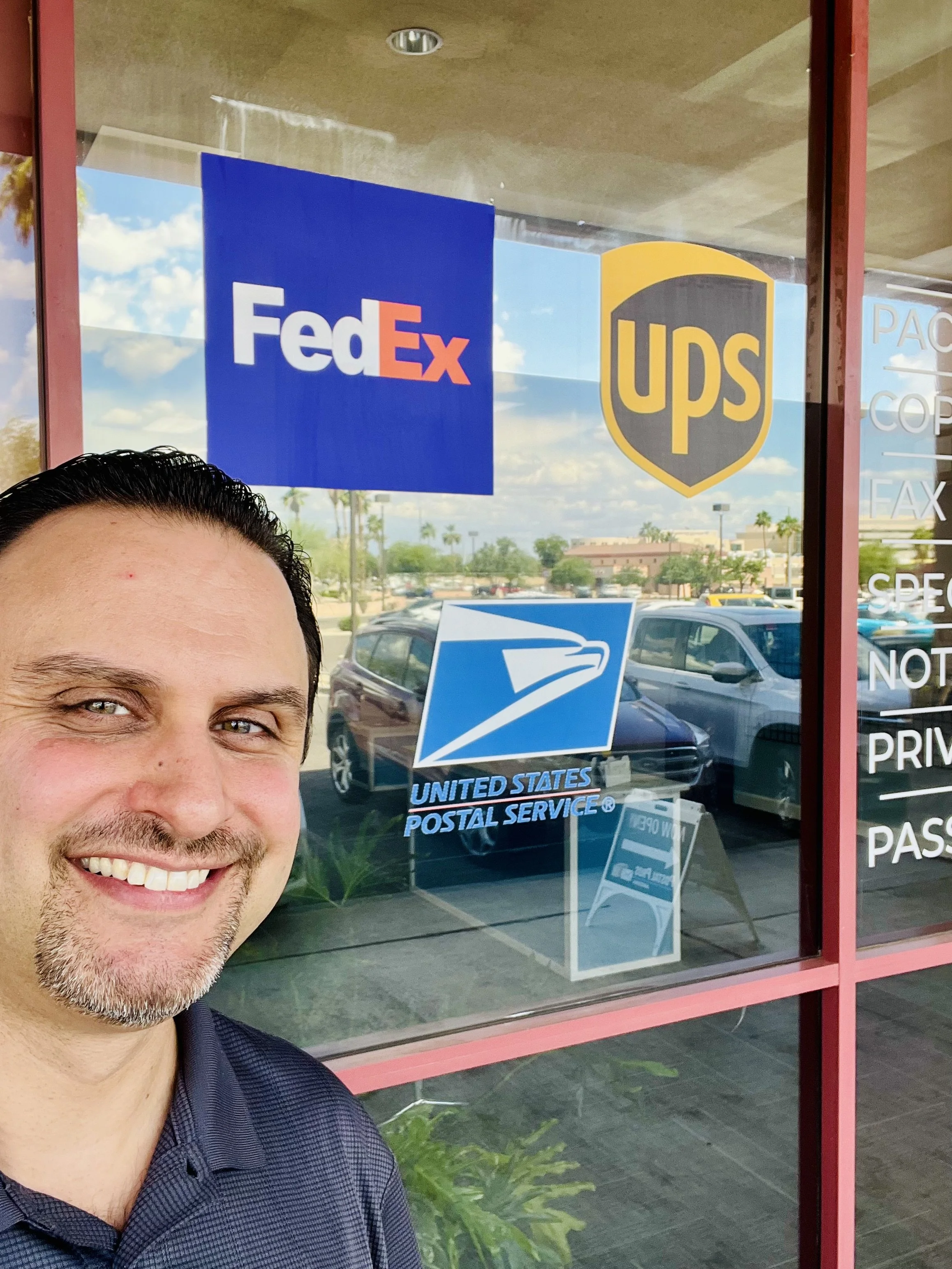 Owner standing in front of FedEx, UPS, and USPS logos