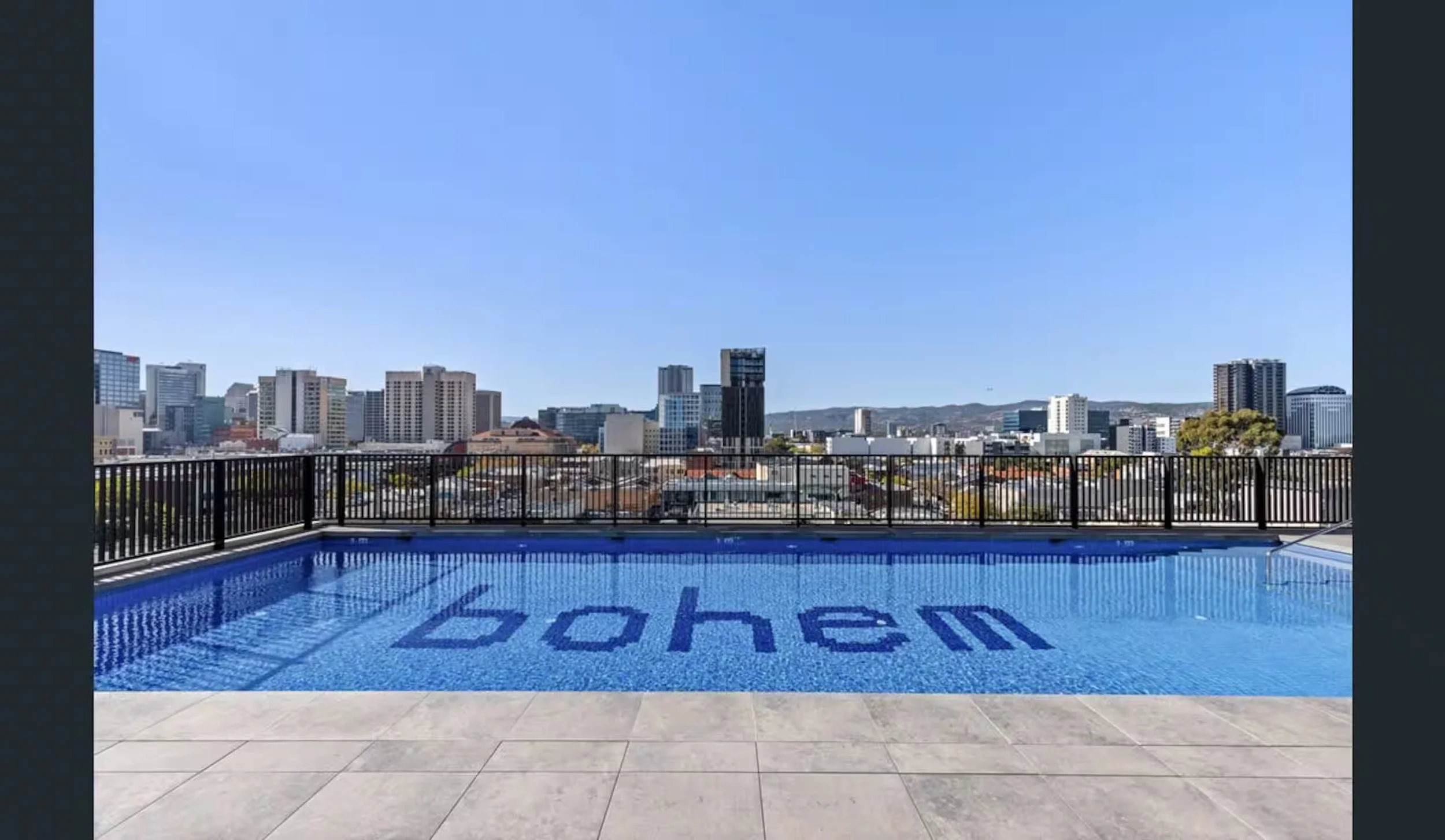 City skyline view from a rooftop pool with the word 'bored' written on the pool floor.
